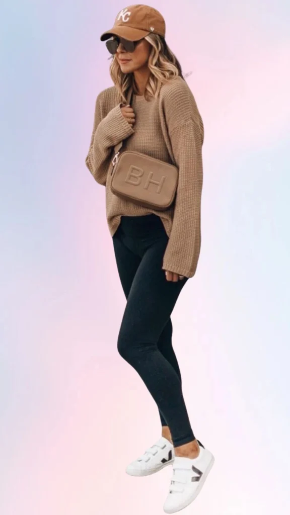 The outfit features an oversized, light brown knit sweater with a relaxed fit, paired with black leggings that offer a snug yet comfortable fit. Completing the look are white sneakers with elastic straps and a casual brown cap, creating a cozy, laid-back style perfect for a lazy day.