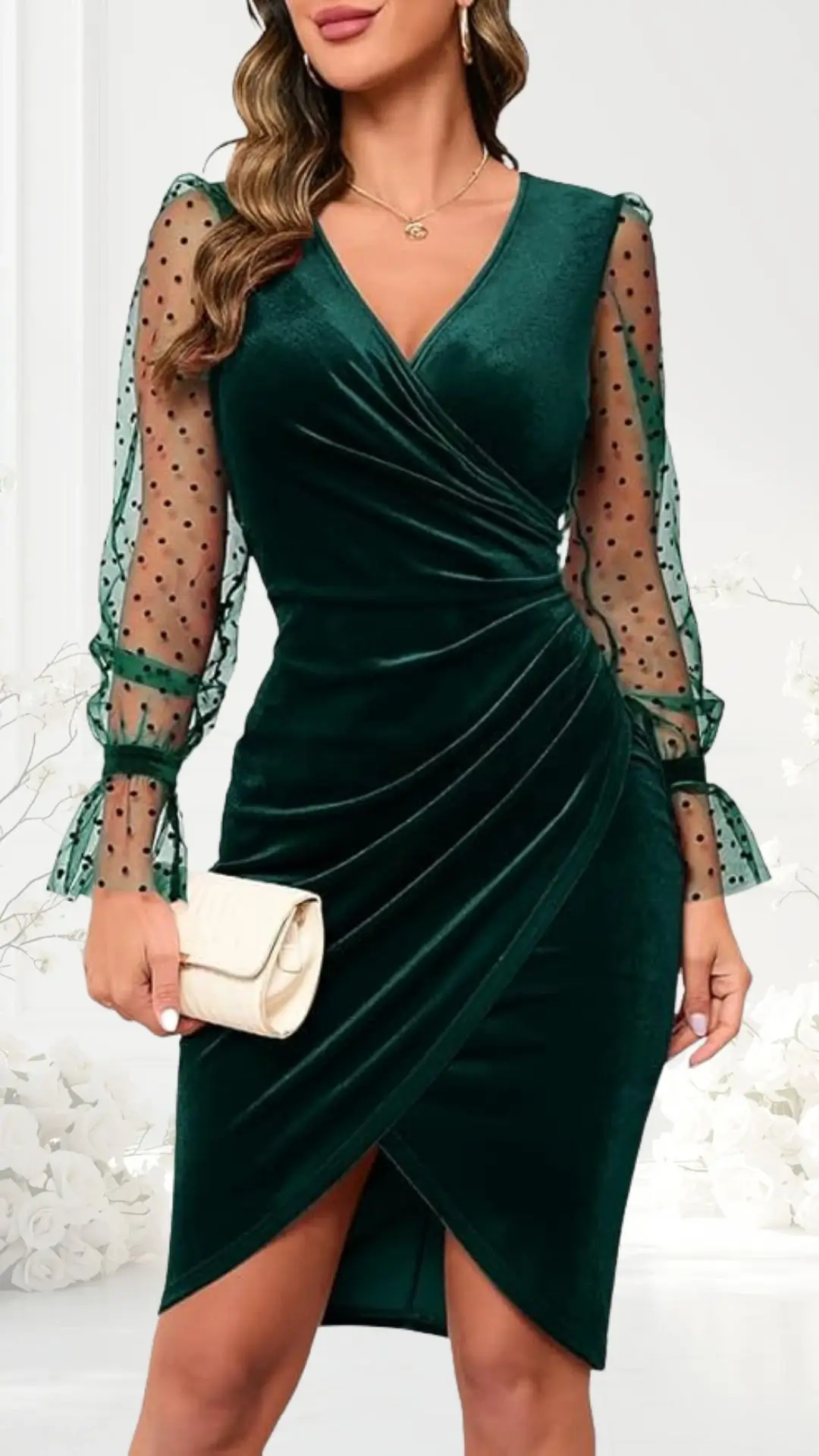 The dress is a deep green cocktail style with a flattering V-neck and a wrap design, featuring soft velvet fabric. The long sleeves are made of sheer mesh adorned with black polka dots, finished with elegant ruffled cuffs. A cream-colored clutch completes the look, enhancing the sophisticated appearance suitable for wedding guests.