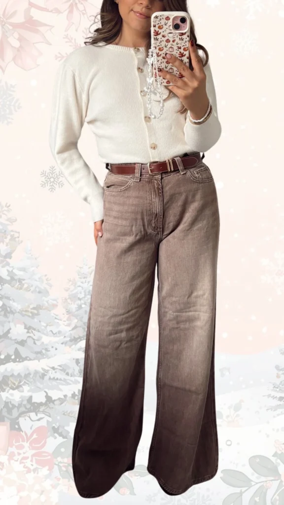 A cozy cream cardigan with ribbed texture features a button-down front, paired with wide-leg brown jeans that have a soft, faded finish. The outfit is cinched at the waist with a brown leather belt, adding a polished touch suitable for winter. Finishing the look, delicate accessories like a beaded necklace complement the ensemble.