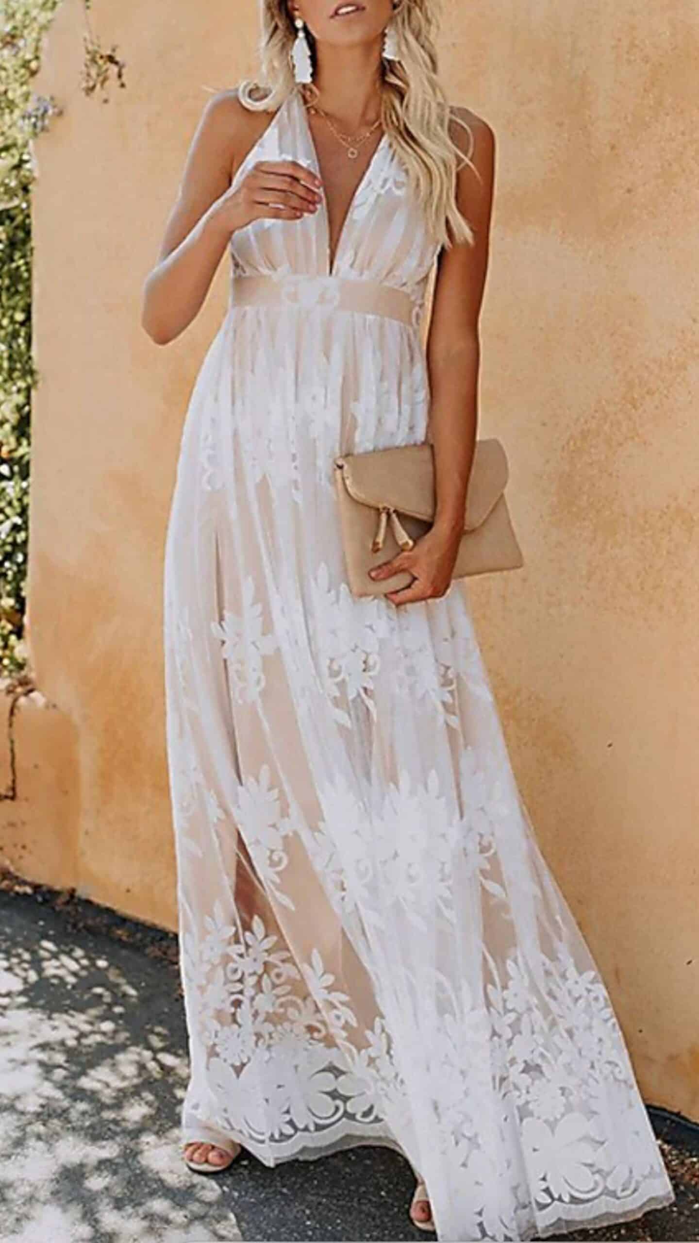 A flowing, full-length white dress features a plunging V-neckline and delicate halter straps, highlighting an elegant silhouette. Made from sheer fabric adorned with floral lace embellishments, it exudes a romantic and ethereal vibe, making it perfect for a formal event or a wedding guest attire.
