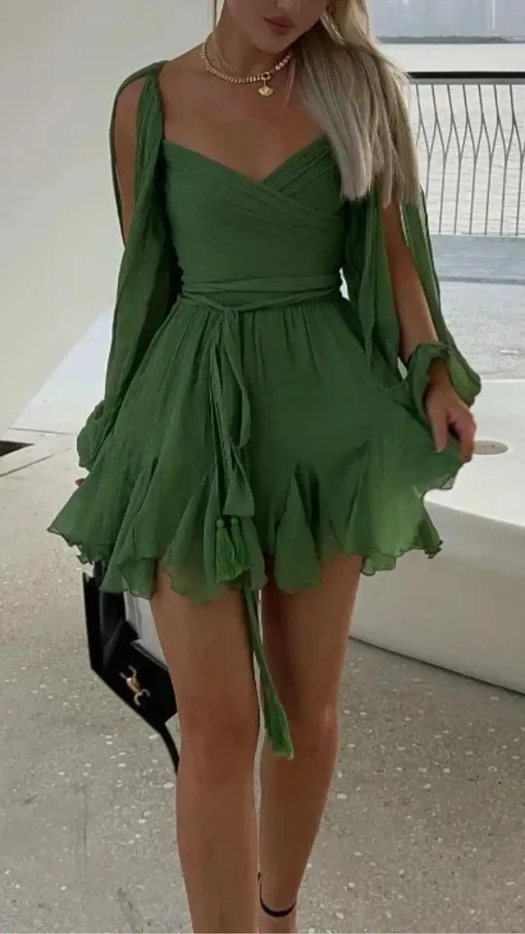 This emerald green homecoming dress features a lightweight, textured fabric that drapes elegantly and has a flirty, voluminous skirt with a ruffled hem. The design includes a fitted bodice with a V-neckline and flowing sleeves, creating a romantic and youthful vibe, perfect for a formal event or school dance.