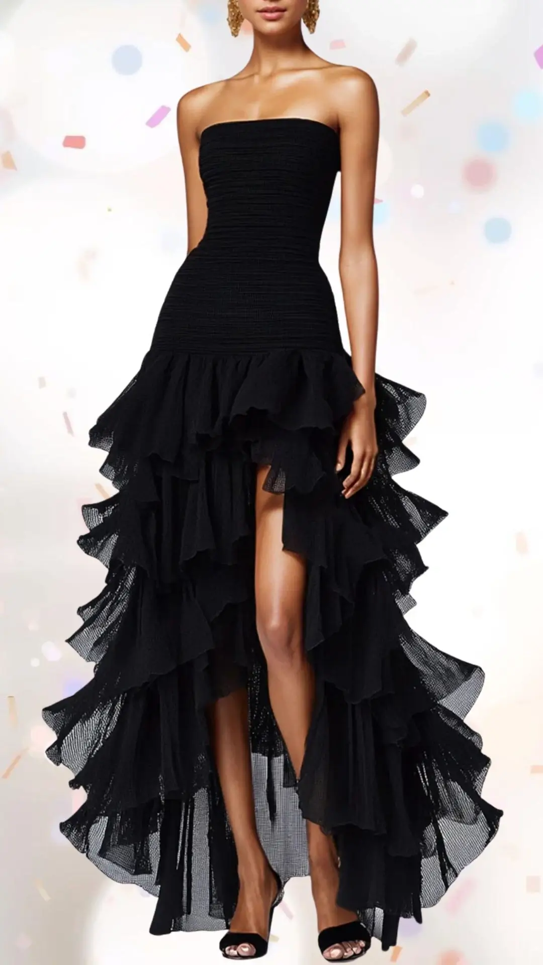 The outfit features a strapless, fitted black dress that combines elegance with playful whimsy, showcasing a cascading ruffle hemline that creates movement and flair. Made from a lightweight fabric with a textured finish, the dress boasts a structured design complemented by its flowing layers, making it suitable for a celebratory occasion. Subtle details, such as the bold silhouette and delicate ruffles, elevate the look while maintaining a fun and approachable vibe.