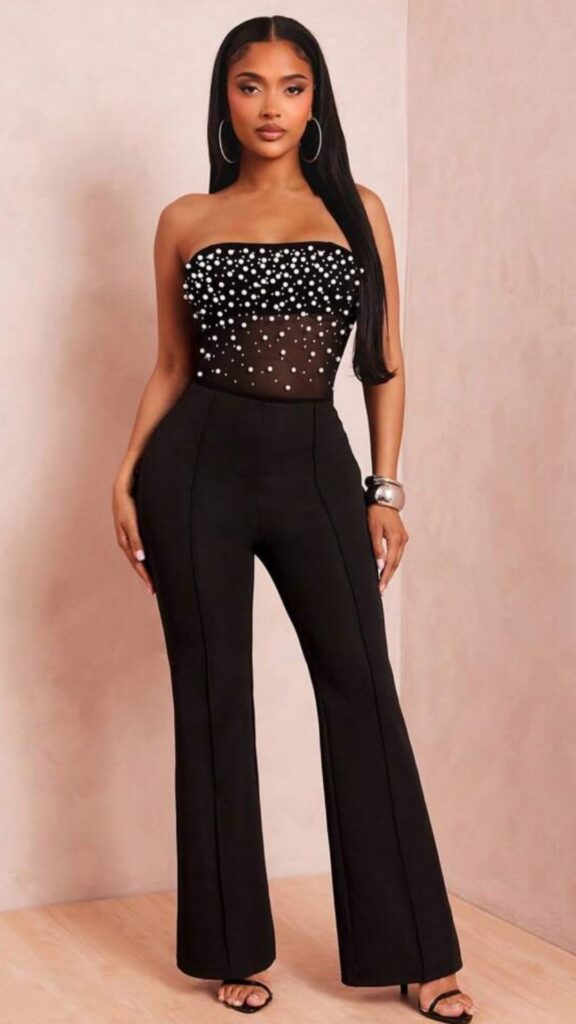 The outfit features a strapless black bodysuit adorned with shimmering embellishments that create an elegant contrast against the sheer fabric. Paired with high-waisted, tailored black flared trousers, the ensemble is both flattering and sophisticated, making it ideal for evening events like birthday parties or date nights. Its sleek design is complemented by minimalistic high-heeled sandals for an elevated finish.