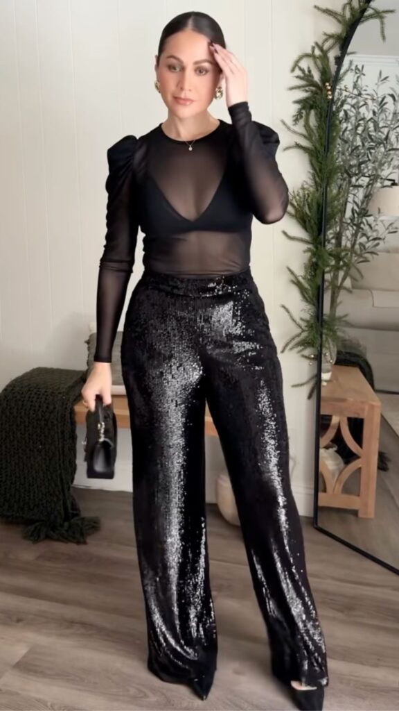 The outfit features a sheer black long-sleeve top with subtle puffed shoulders, providing an elegant yet bold silhouette, paired with high-waisted black sequin trousers that flow fluidly to the floor, creating a dazzling effect with their reflective surface. Accessorized with a compact black handbag and simple hoop earrings, this ensemble is perfect for classy occasions like birthday parties or date nights. The combination of fabrics and tailored fit enhances the outfit's sophisticated appeal while maintaining comfort.