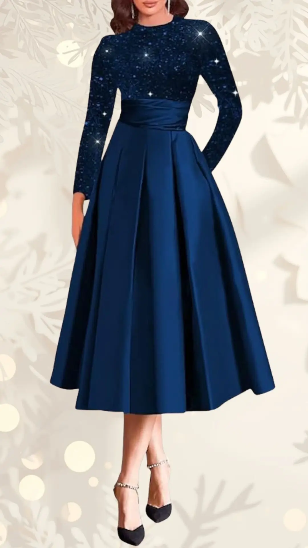 The dress features a fitted, glittering navy blue bodice with long sleeves, transitioning into a flowing, pleated skirt that falls below the knee. A satin waistband cinches the waist, creating an elegant silhouette, complemented by stylish black heels adorned with ankle straps. The background is softly blurred with a floral pattern, enhancing the festive theme of the outfit.