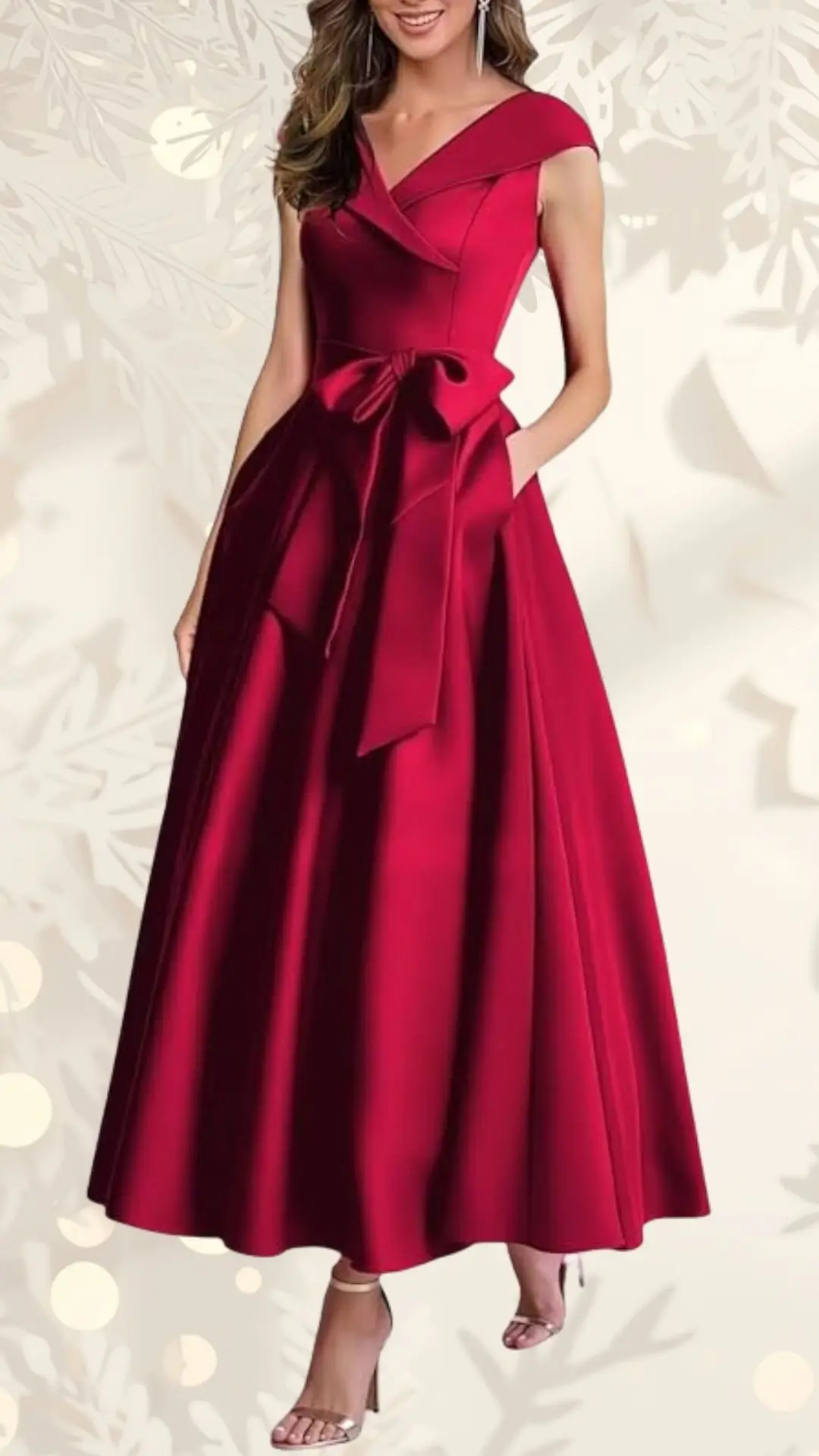 The image features a festive red wedding guest dress with a fitted bodice and a stylish wrap-around neckline. The gown flows into a full-length skirt, accentuated by a matching satin bow at the waist, and the model pairs it with strappy metallic heels. The background is softly blurred to keep the focus on the dress.