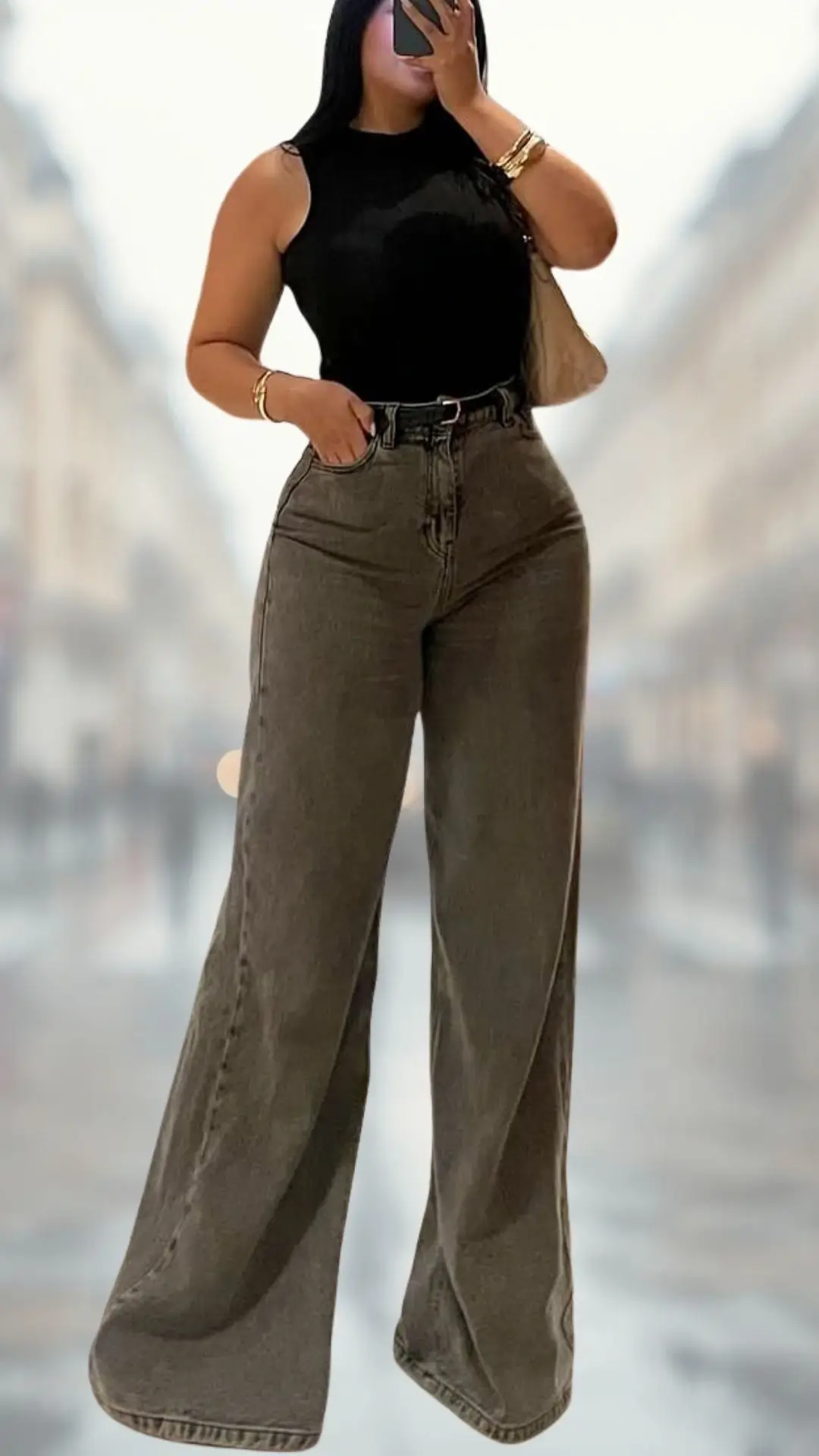 The outfit features a form-fitting sleeveless black bodysuit made from a smooth, stretchy fabric, paired with high-waisted flare jeans in a rich, dark gray denim. The jeans are wide-legged, providing a dramatic silhouette, and the look is complemented by subtle gold accessories, enhancing the overall polished appearance.
