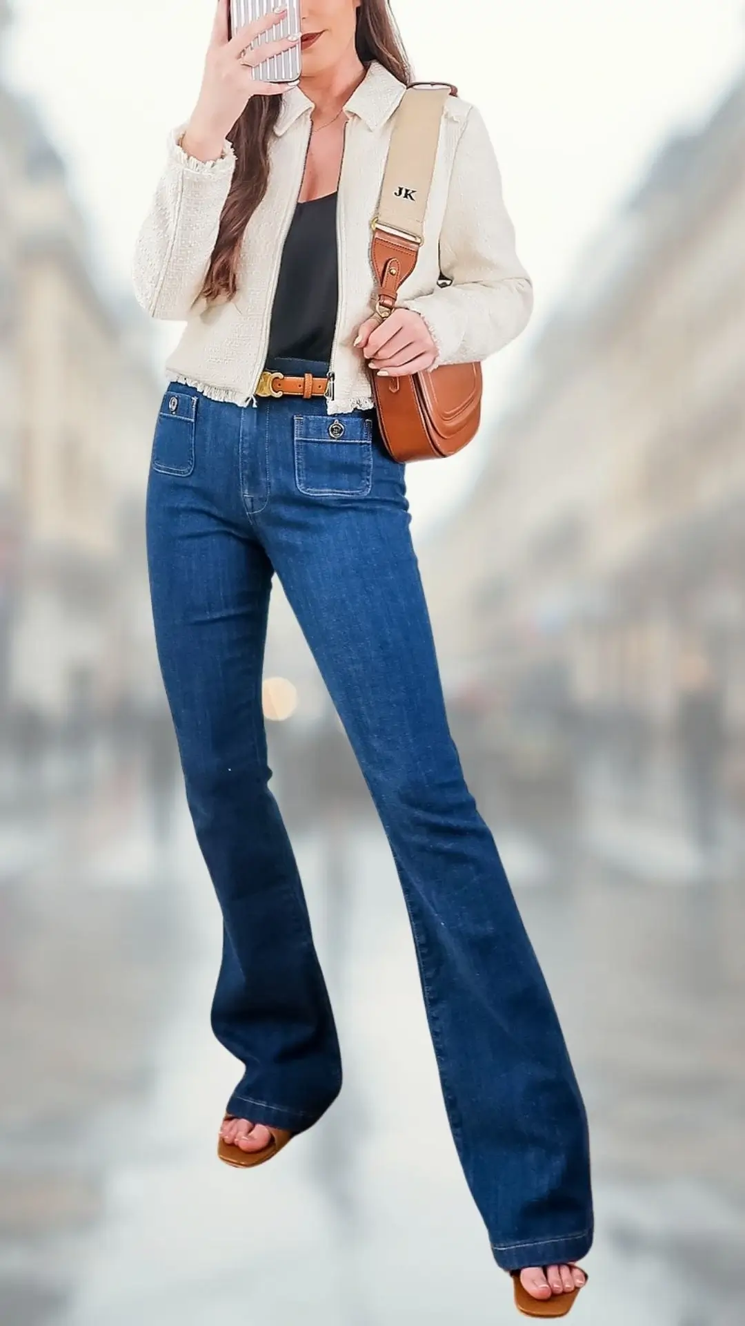 The outfit features light beige flare jeans made from soft denim, complemented by a fitted black tank top. A textured, cropped cream jacket adds dimension, while a brown belt accentuates the waist; the ensemble is finished with stylish brown heeled sandals, creating a chic and sophisticated look suitable for various occasions.