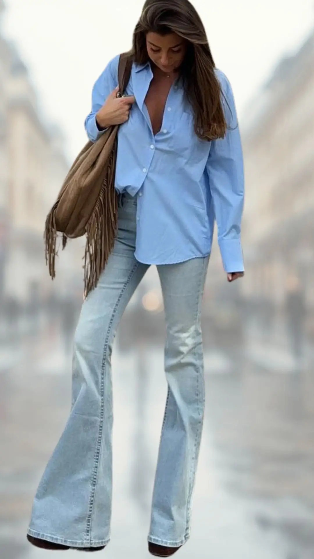 A light blue, oversized button-up shirt is paired with high-waisted, faded flare jeans, creating a relaxed yet stylish silhouette. The outfit is complemented by brown platform boots and a fringed tan shoulder bag, adding texture and a bohemian touch. The overall look is casual and chic, perfect for a fashionable day out.