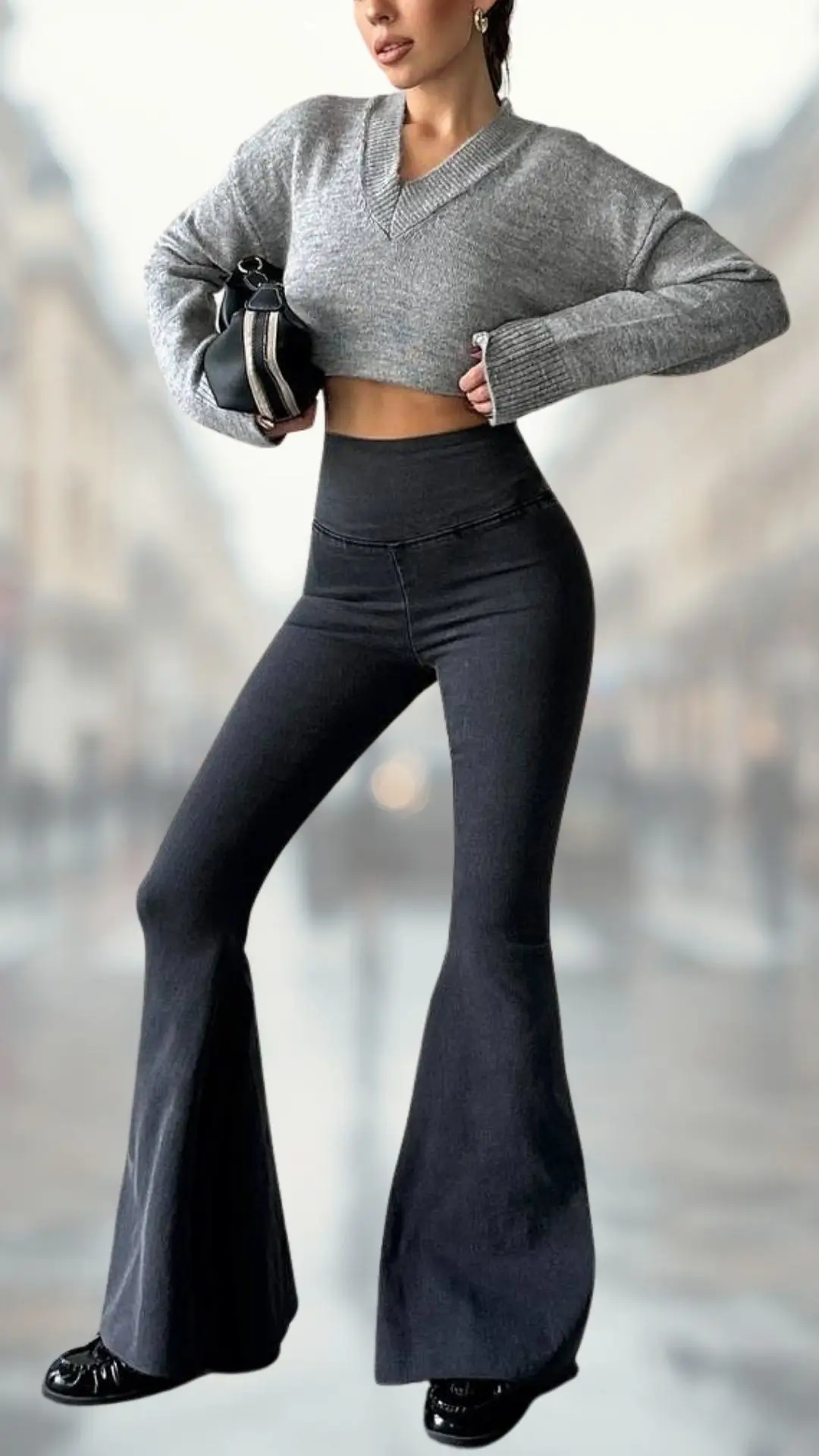 A cropped, gray knitted sweater features a deep V-neck and long, slightly flared sleeves, paired with high-waisted black flare jeans made from a sleek denim fabric. The outfit is completed with shiny black shoes that accentuate the modern silhouette, creating a stylish and contemporary look.