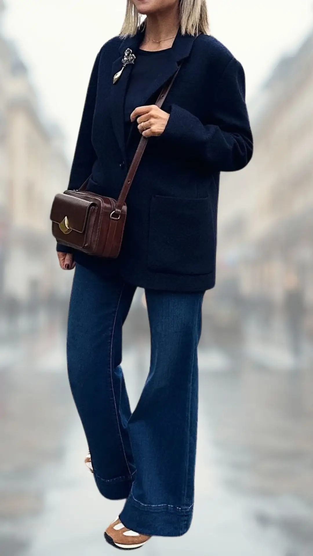 The outfit features a tailored navy blazer with a relaxed fit, paired with high-waisted flare jeans in a rich denim fabric. Completing the look are stylish beige heeled sandals, with a woven texture detailing on the straps, and a coordinating brown crossbody bag adorned with a subtle gold clasp.
