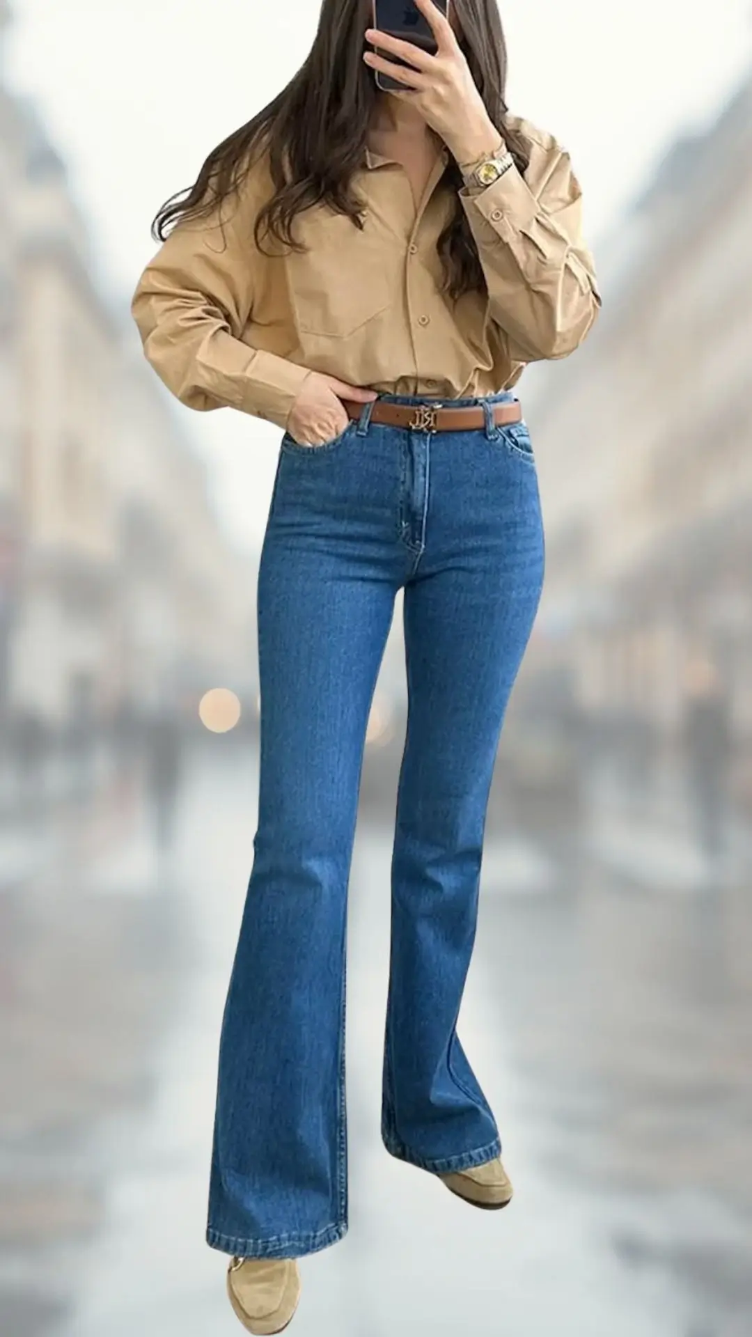 The outfit features a light beige, oversized button-up shirt with long sleeves, paired with high-waisted blue flare jeans in a medium denim wash. Complementing the look, light tan shoes enhance the overall aesthetic while a brown belt adds definition to the waist, creating a chic and stylish ensemble.