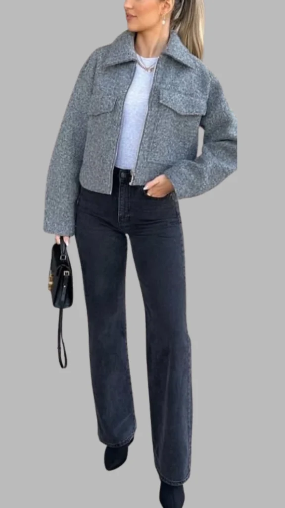 The outfit features a cropped, textured grey jacket with large front pockets and a classic collar, paired with high-waisted, dark denim jeans that offer a flattering silhouette. The look is completed with sleek black ankle boots, creating a chic and modern ensemble suitable for various occasions. The mix of soft grey tones and deep black emphasizes a trendy monochromatic aesthetic.