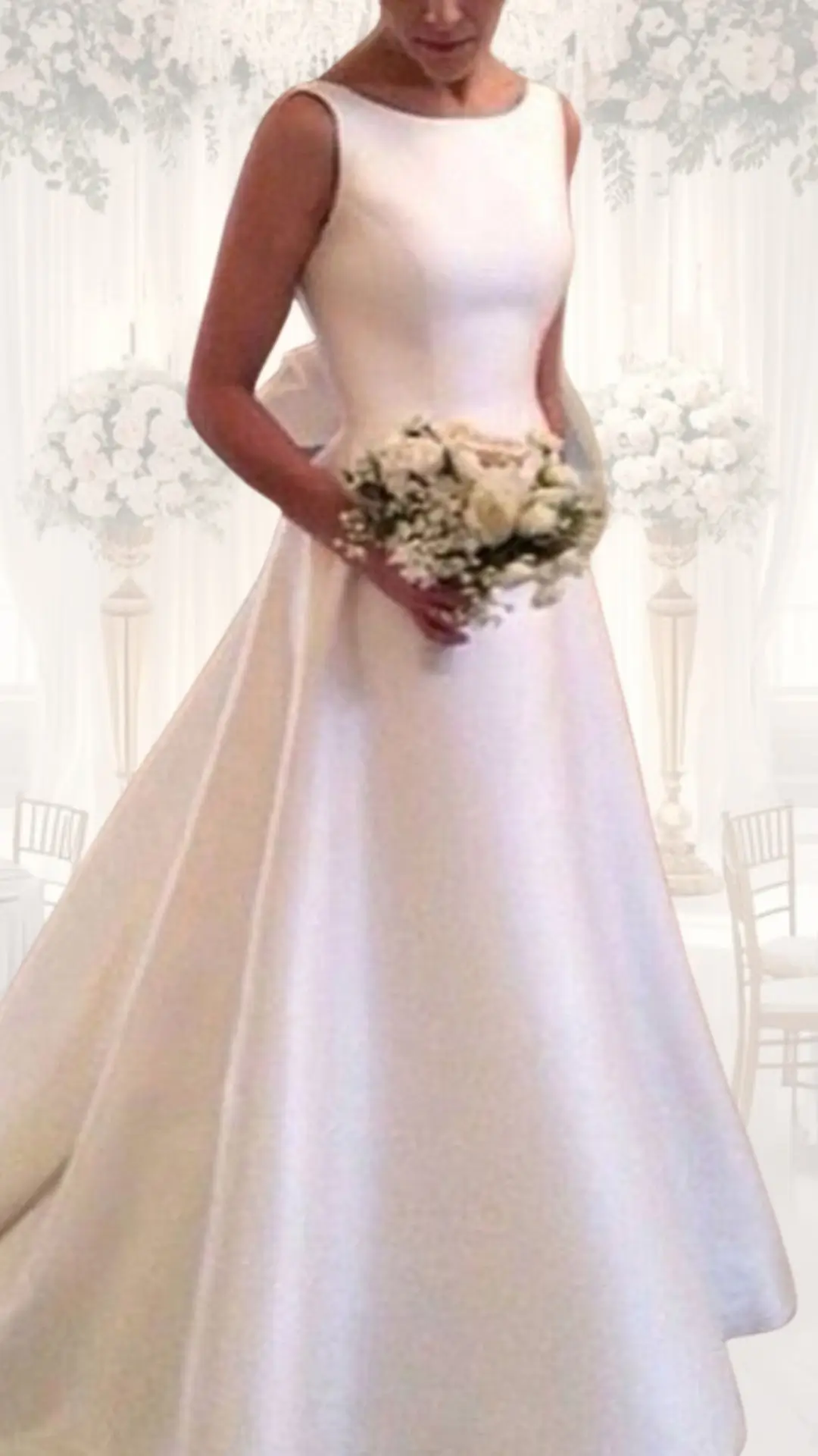 The high neck wedding gown features a timeless silhouette crafted from a luxurious, heavy fabric that drapes beautifully. It showcases a sleeveless design with a simple, elegant neckline, while the skirt flows into an A-line shape, enhancing its modest yet sophisticated look, perfect for a winter or vintage wedding. The subtle sheen of the fabric adds a touch of opulence, complemented by the bride's delicate bouquet of white flowers.