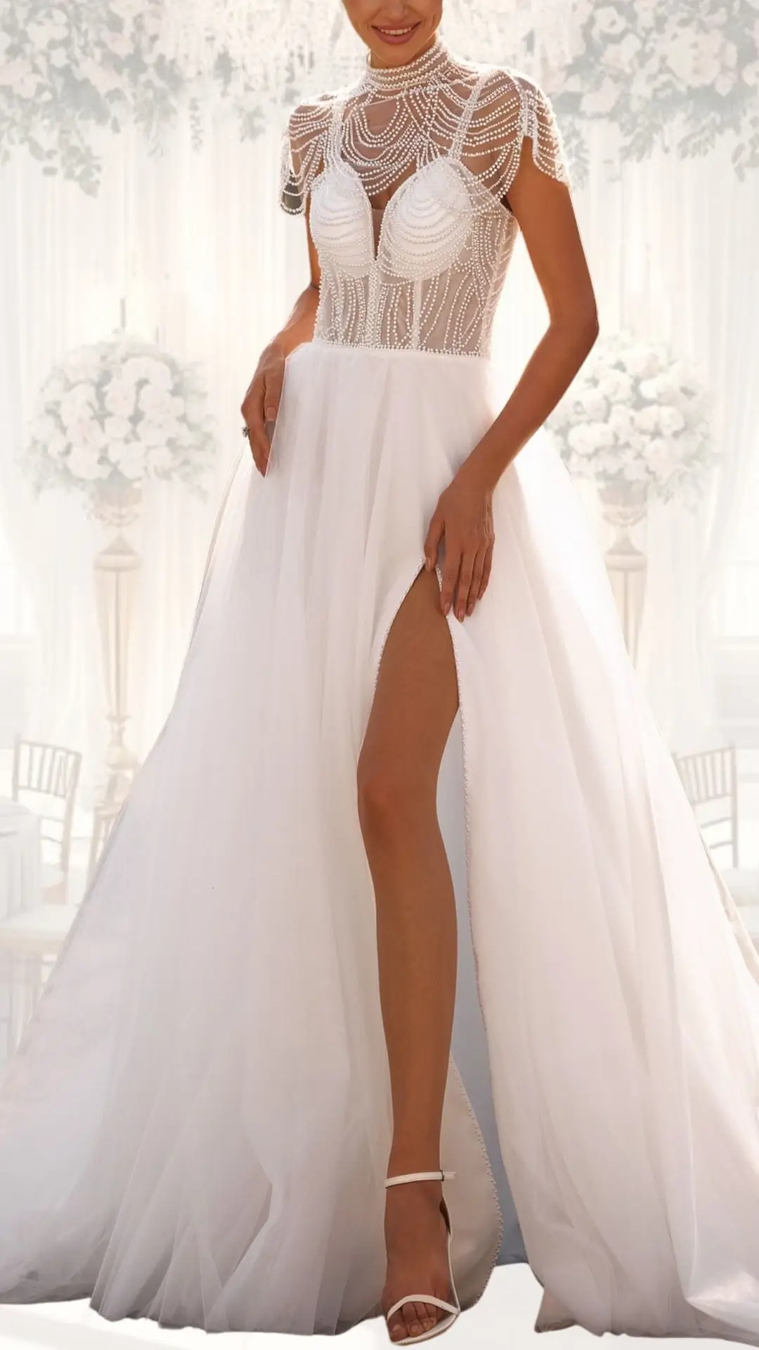 This high neck wedding gown features a fitted bodice adorned with intricate beadwork and a sheer overlay, complemented by cap sleeves for an elegant touch. The flowing skirt, made of soft tulle, presents a sophisticated slit, enhancing its vintage vibes while maintaining a classy and modest silhouette. The gown's pure white shade and luxurious textures make it an ideal choice for a winter wedding.