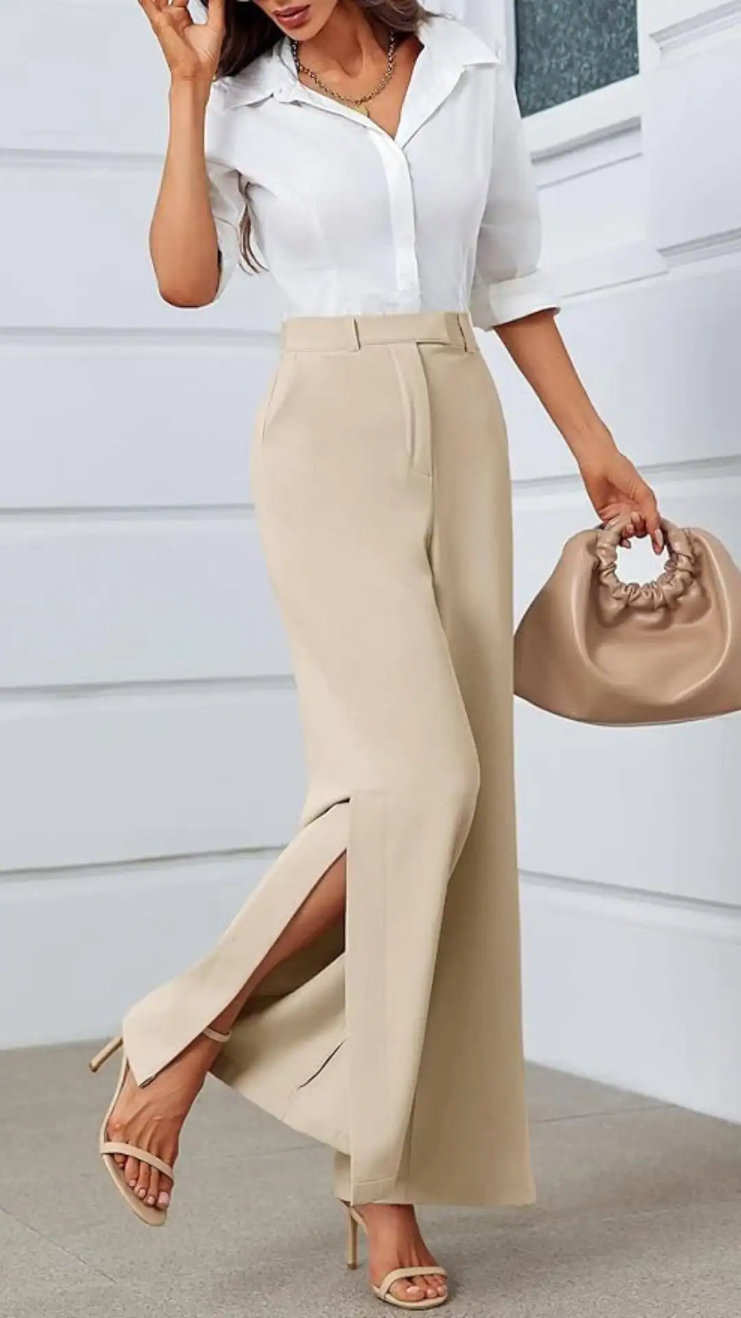 This outfit features high-waisted, wide-leg pants in a soft beige fabric that exhibits a slight sheen, providing a sophisticated and modern silhouette. The design includes a subtle side slit, enhancing movement and pairing elegantly with a crisp white button-up shirt for a polished look suitable for casual outings or office wear.