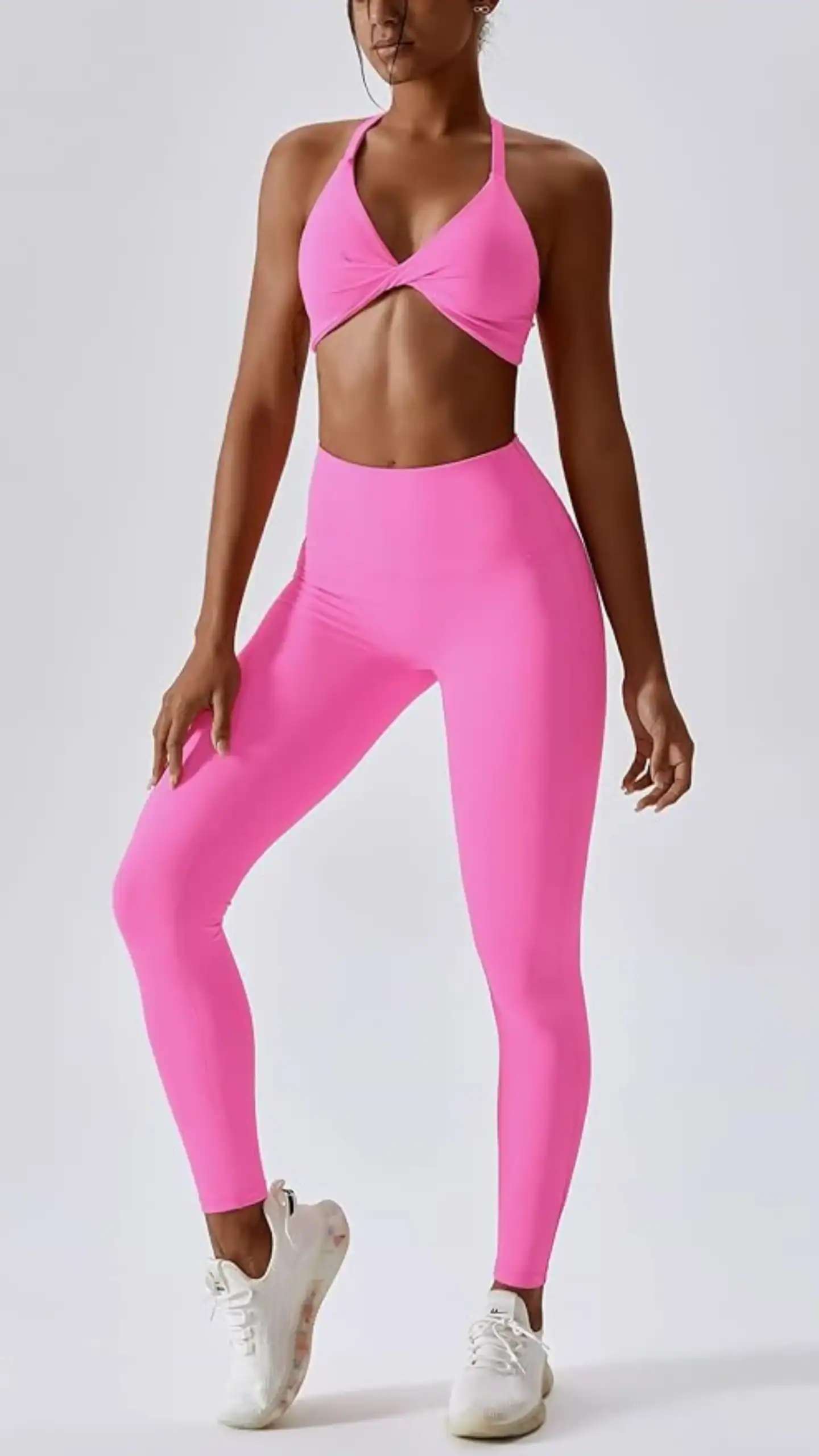 A vibrant, hot pink matching workout set featuring a twist-front sports bra with removable padding and crossed back straps, paired with high-waisted leggings for tummy control and a butt-lifting effect. Made from a buttery soft, 4-way stretch fabric, this bold athleisure ensemble is perfect for various activities like yoga, running, and gym workouts, exuding a youthful and energetic vibe.