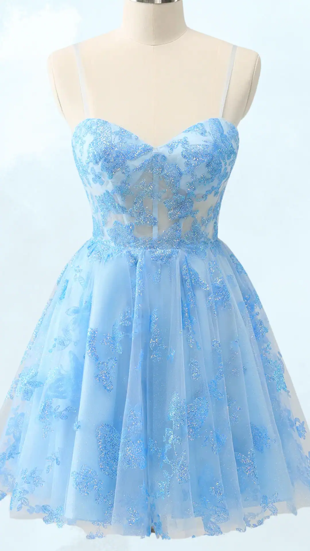 This enchanting light blue homecoming dress features a fitted bodice with delicate and sparkling floral appliqués over a sheer fabric, complemented by a voluminous skirt that falls gracefully at mid-thigh. Designed with thin spaghetti straps, it exudes a whimsical and fairy-tale vibe, making it perfect for teenage girls attending formal events like homecoming or prom.