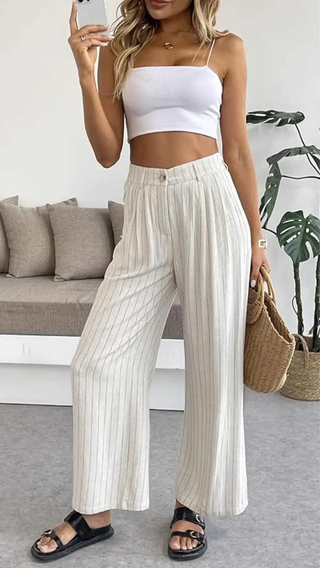 This outfit features lightweight, breathable linen pants with a relaxed fit, showcasing subtle vertical stripes in a soft, neutral color palette. Paired with a simple white cropped tank top and flat black sandals, the overall vibe is casual and chic, perfect for a laid-back summer outing or brunch.