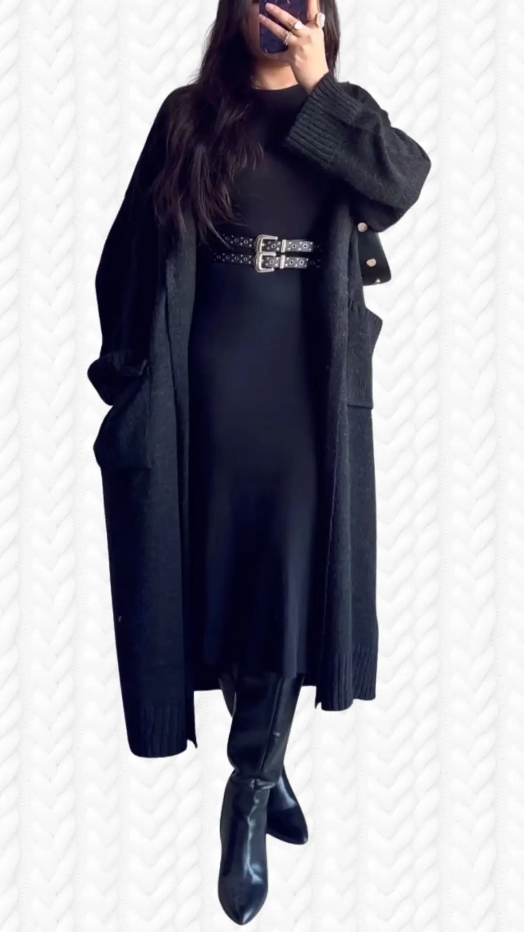 The outfit features a long, open-front cardigan in a soft, textured black knit with ribbed cuffs and patch pockets. Underneath, a sleek black dress is cinched at the waist with a studded black belt, complemented by pointed-toe knee-high black boots that add an elegant flair. The ensemble seamlessly blends comfort and style, perfect for various occasions.