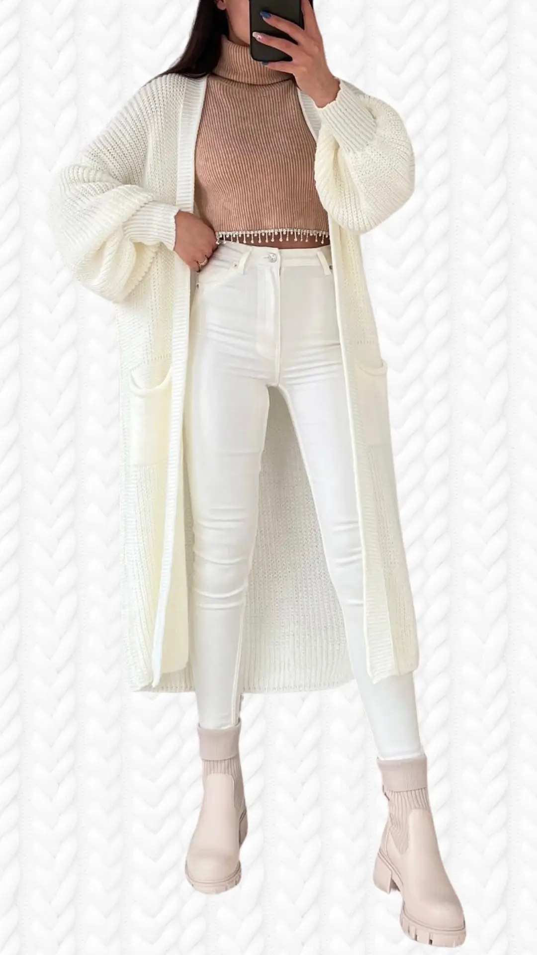 The outfit features an oversized, long cardigan in a soft, textured cream fabric with wide sleeves, layered over a fitted, ribbed turtleneck sweater in a warm beige shade. Paired with high-waisted, slim white pants and stylish blush ankle boots, the ensemble combines comfort and chic style, emphasizing a modern aesthetic. The cardigan includes pockets for added functionality, enhancing its appeal.