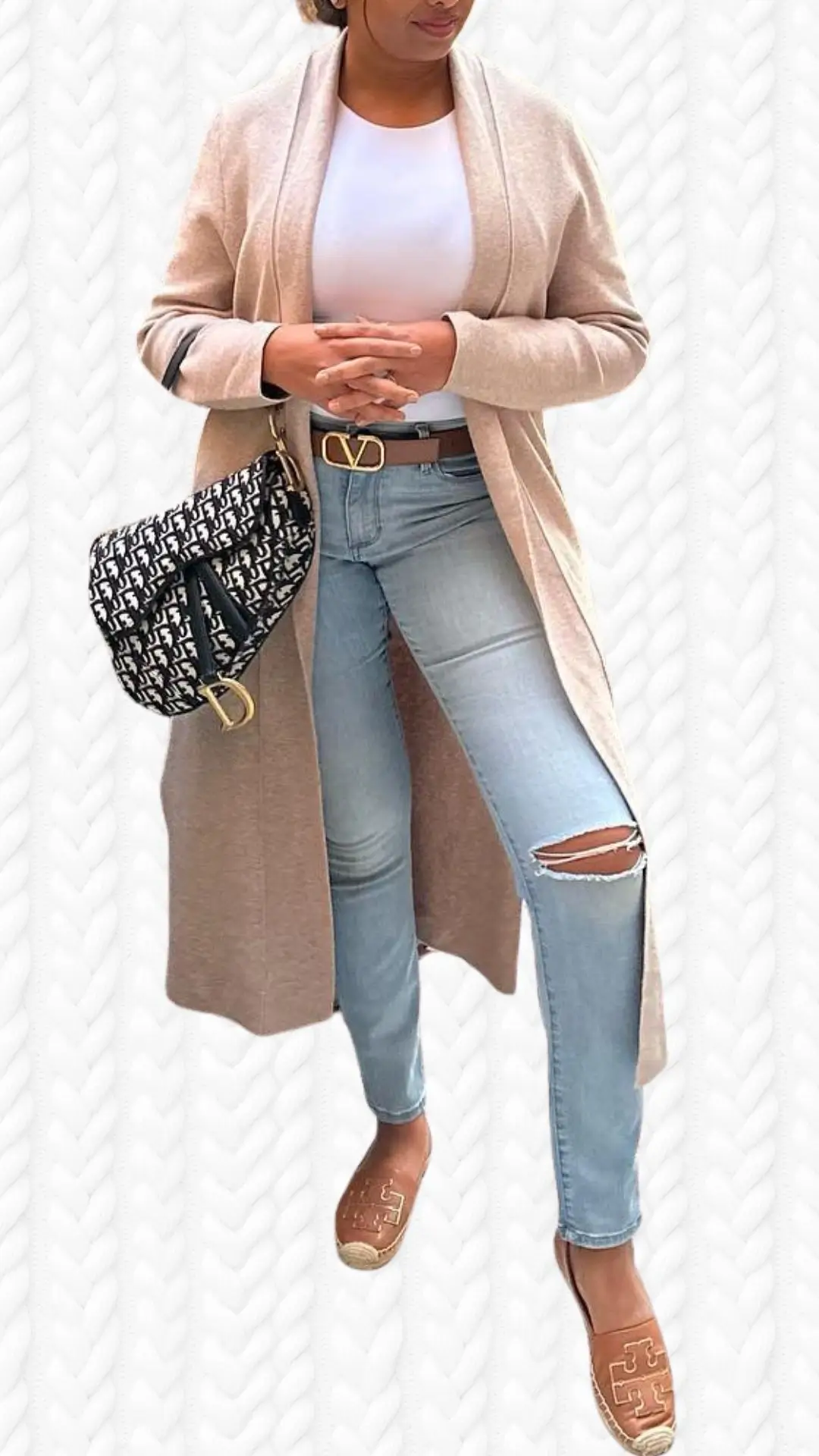 A long, soft beige cardigan drapes elegantly over a white fitted top, featuring a shawl collar and open front. The outfit is paired with light blue skinny jeans that have distressed detailing at the knees, and stylish brown espadrille flats with a logo accent. A chic black and white patterned handbag adds a touch of contrast, completing this fashionable ensemble.