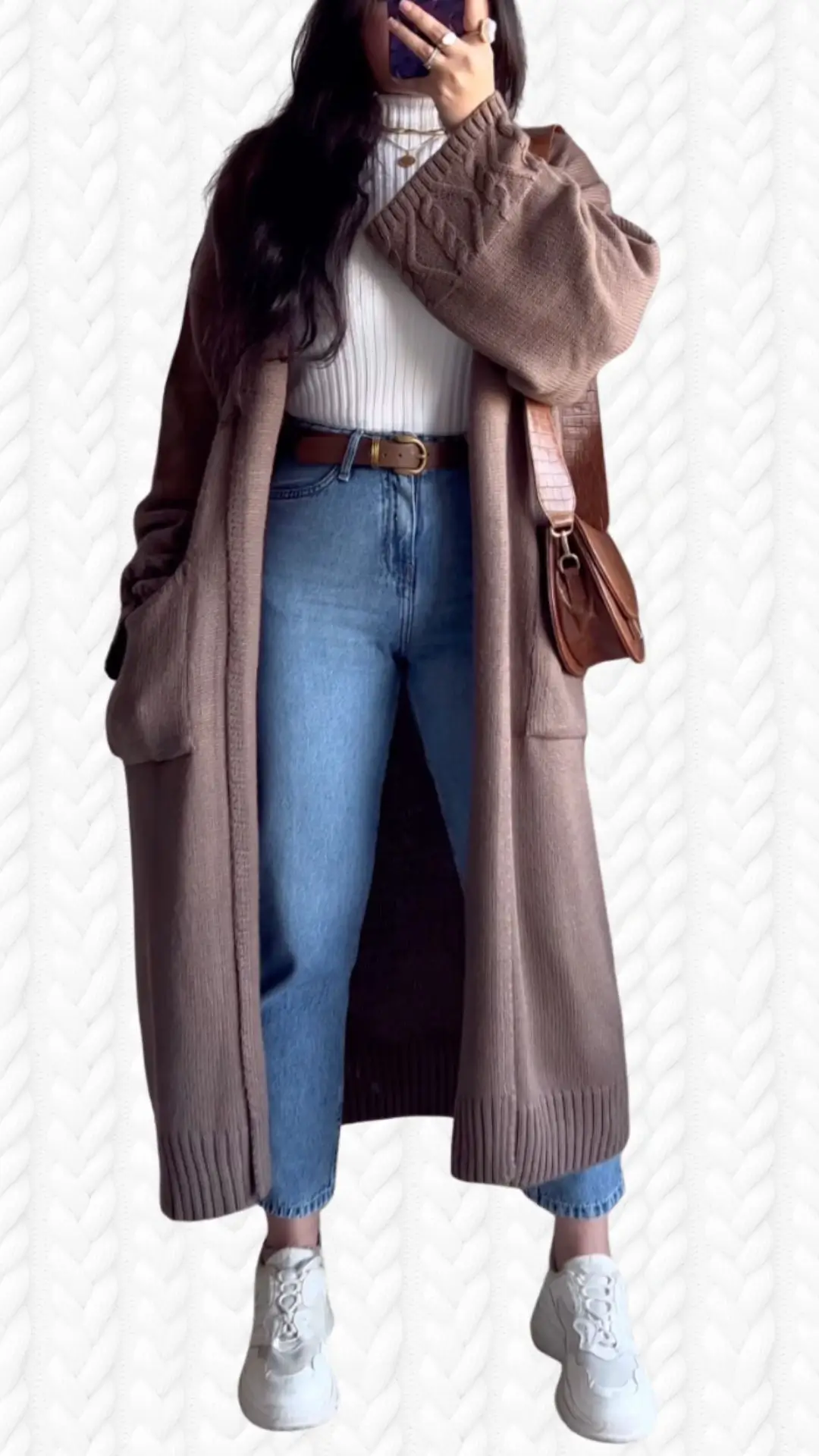 The outfit features a long, cozy cardigan in a soft brown knit with textured sleeves and ribbed detailing at the cuffs and hem, layered over a fitted white ribbed turtleneck. Paired with light blue high-waisted jeans and white sneakers, the ensemble is both stylish and comfortable, complemented by a brown leather crossbody bag.