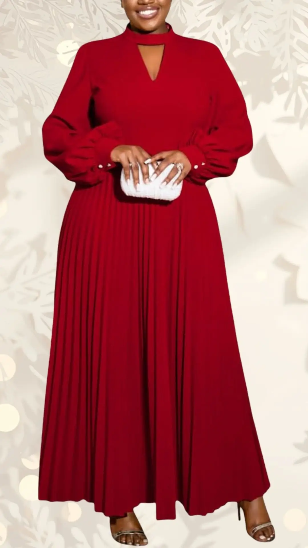 A long sleeve, pleated wedding guest dress in rich red, featuring a high neckline with a keyhole cutout and voluminous sleeves. The dress flows gracefully to the floor, complemented by a model holding a textured white clutch. She wears elegant silver strappy heels, enhancing the formal look.
