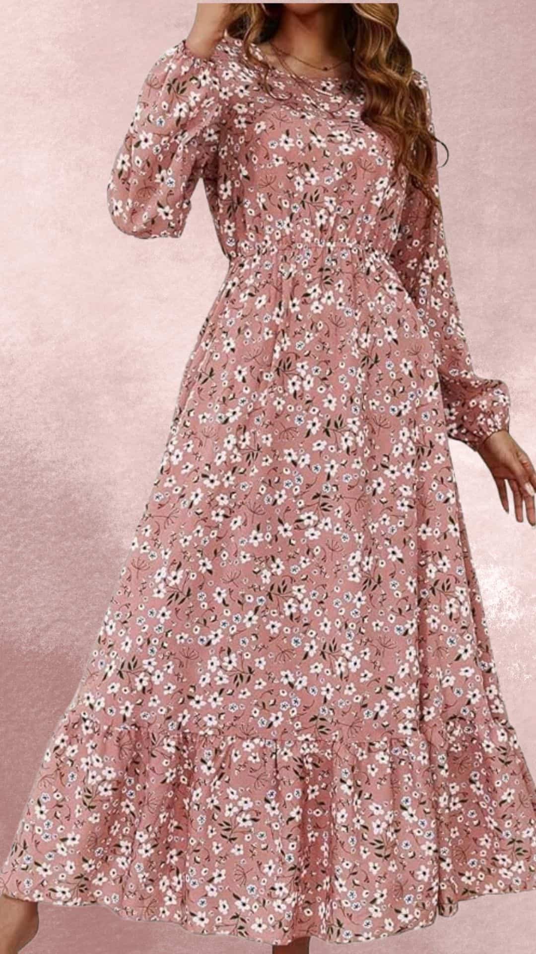 A flowy maxi dress in a soft blush tone features a delicate floral pattern with white and blue blossoms against a leafy backdrop. The dress has long, billowy sleeves and an elasticized waist, providing a comfortable fit, while the ruffled hem adds a romantic touch, perfect for pairing with cowboy boots for an elegant country western look.