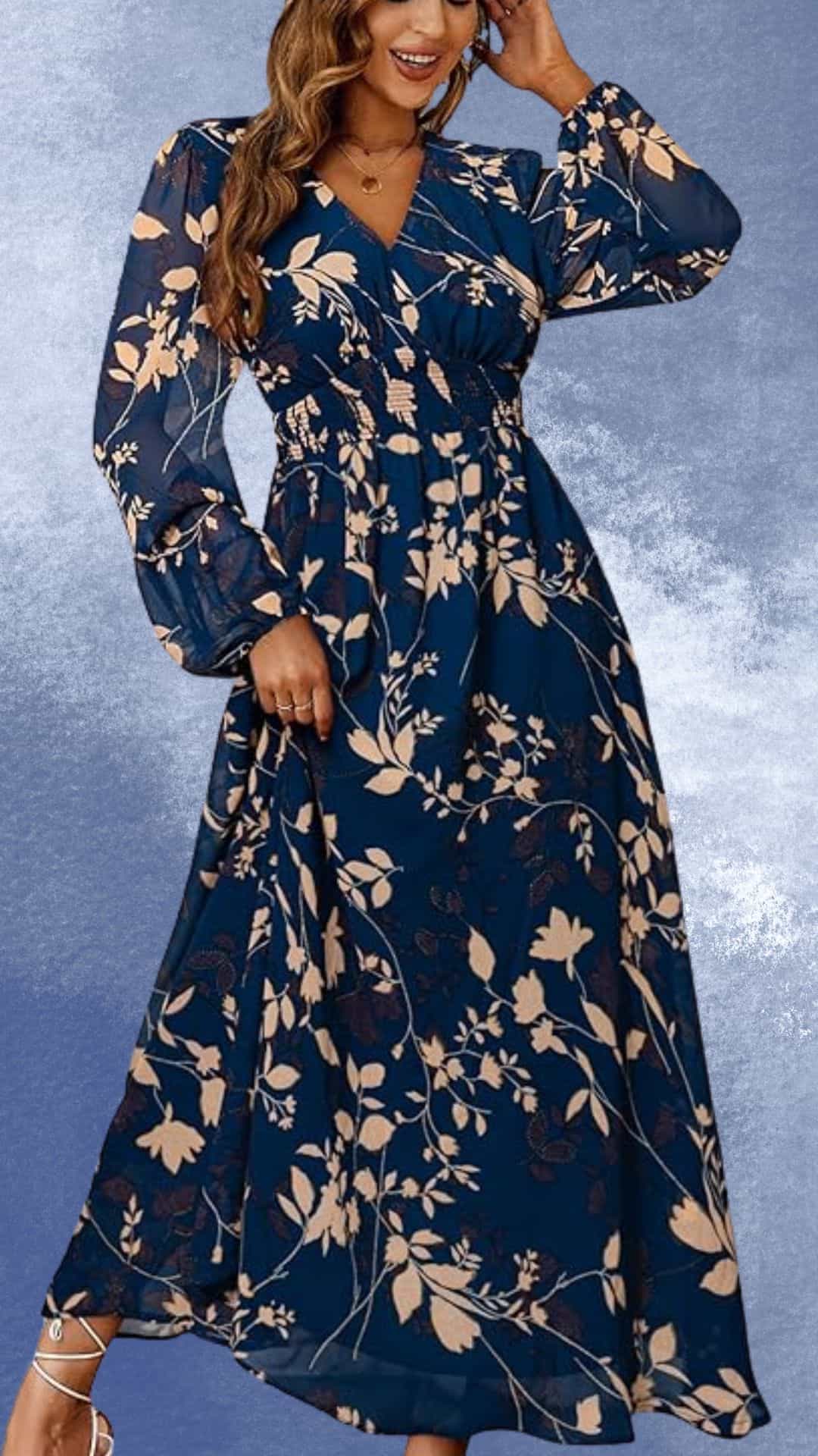 A flowing maxi dress features a deep navy background adorned with delicate blush pink floral patterns, exuding an elegant country western vibe. The dress has long, billowing sleeves and a flattering wrap-style bodice that enhances the natural waistline, making it a perfect choice to complement cowboy boots. The skirt cascades gracefully, offering movement and lightness, ideal for both casual outings and dressed-up occasions.
