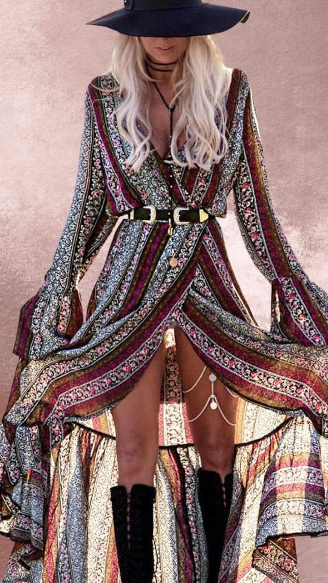 This maxi dress features a flowing, multi-patterned fabric with rich burgundy and teal hues, complemented by an elegant belt at the waist. The long sleeves and ruffled hem enhance its western charm, while a high slit reveals stylish black cowboy boots. A wide-brimmed hat adds a finishing touch, perfect for a country-western aesthetic.