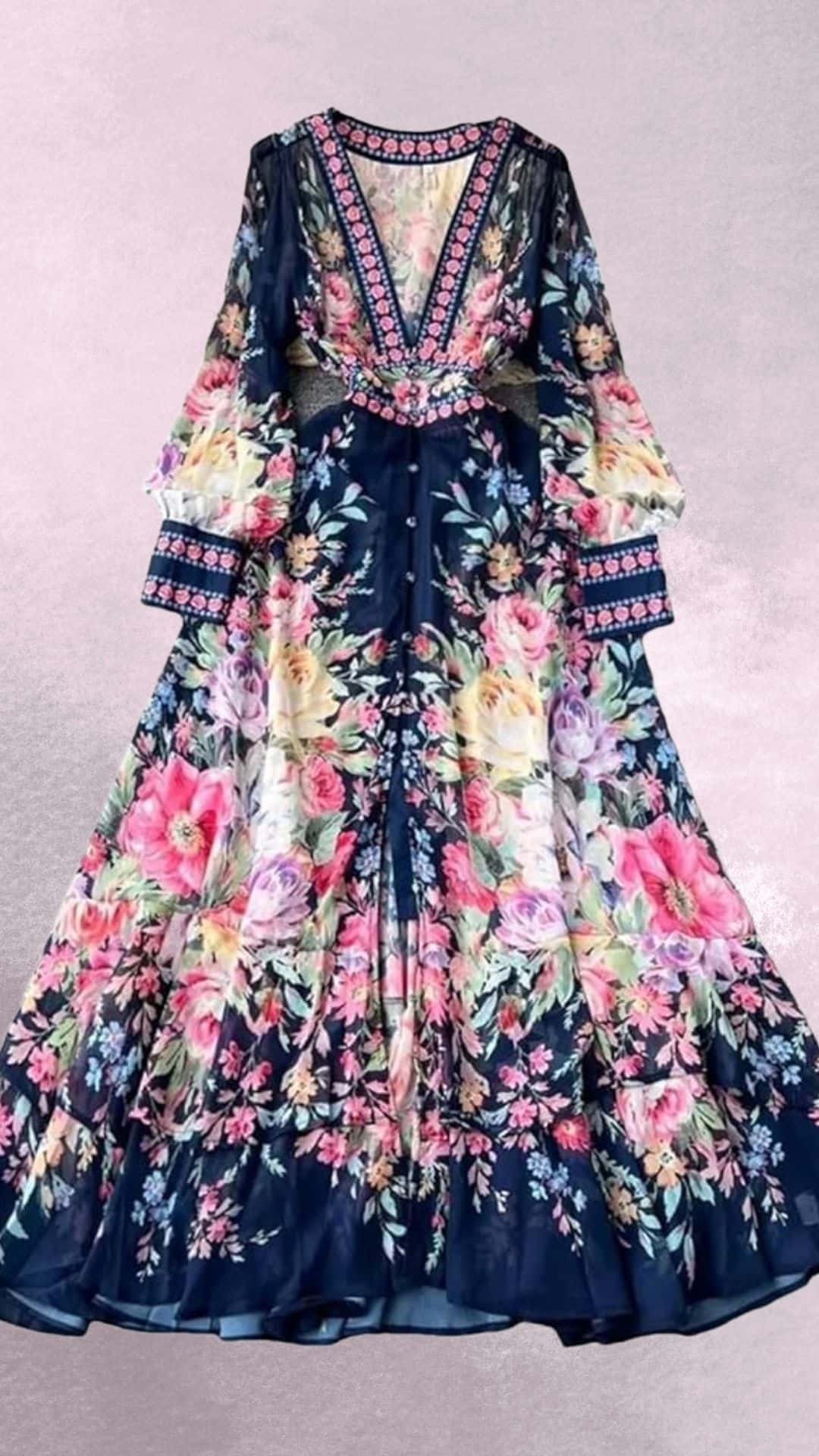 A flowing navy maxi dress adorned with vibrant floral patterns in shades of pink, yellow, and lavender features a deep V-neckline and bell sleeves, accentuated by intricate embroidered trim along the neckline and cuffs. The dress has a cinched waist, creating an elegant silhouette that pairs beautifully with cowboy boots for a stylish country western vibe. Its lightweight fabric adds a graceful movement, perfect for warm weather occasions.