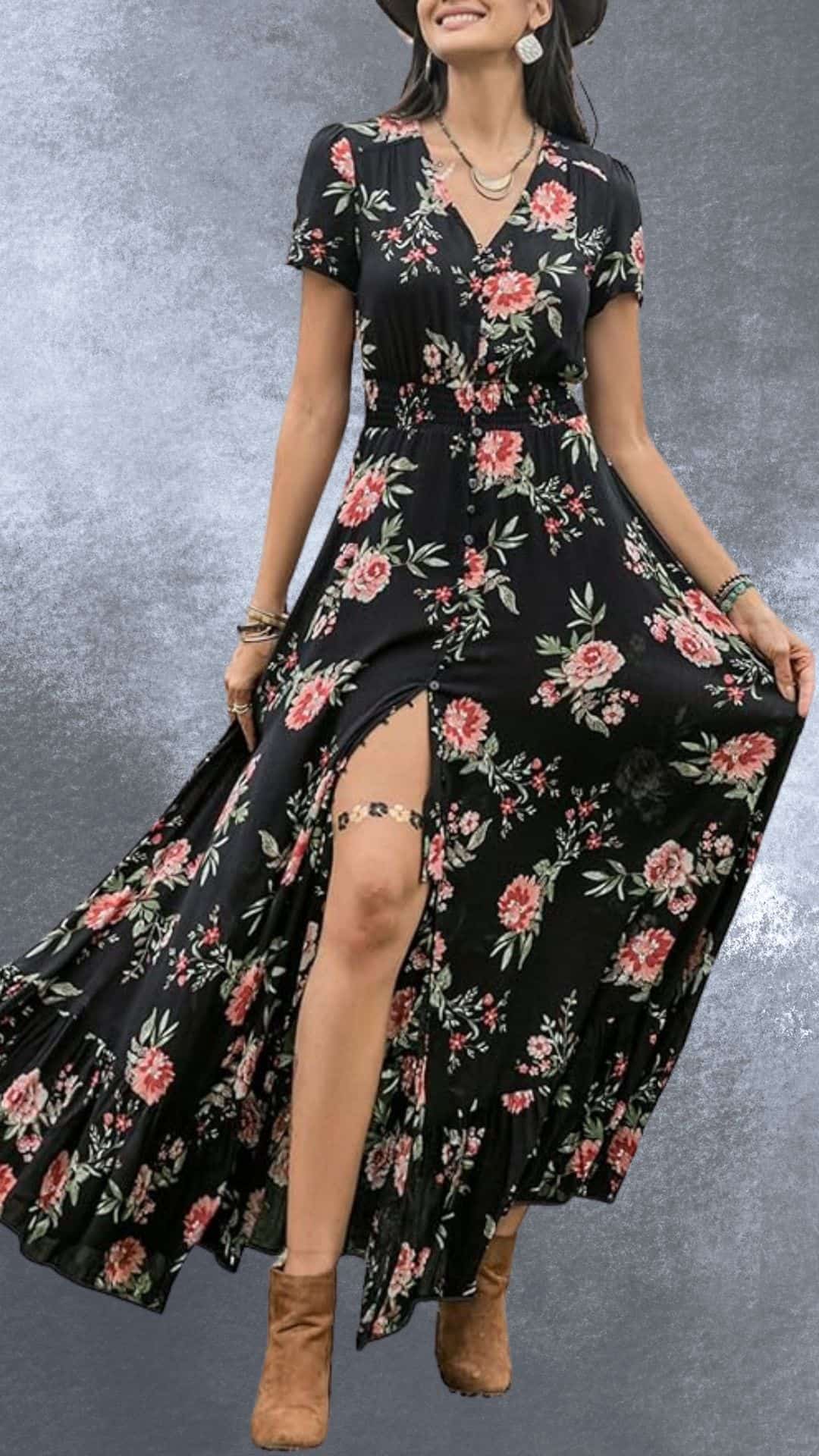A flowing black maxi dress adorned with vibrant floral patterns in shades of pink and green evokes a country western vibe. It features short sleeves and a high slit, allowing graceful movement, while the model complements it with tan cowboy boots. This stylish combination is perfect for a chic yet relaxed outdoor gathering or event.