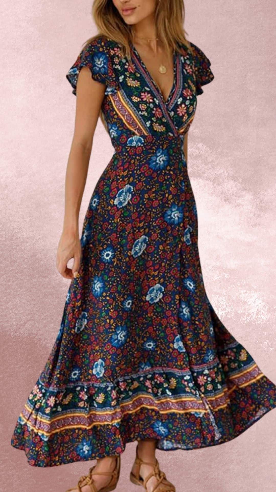 The dress features a deep V-neckline and flutter sleeves adorned with a vibrant floral print in shades of blue, red, and green against a dark background. The flowing maxi length accentuates a bohemian style, while the contrasting striped hem adds a structured, country western vibe, making it a perfect match for cowboy boots.