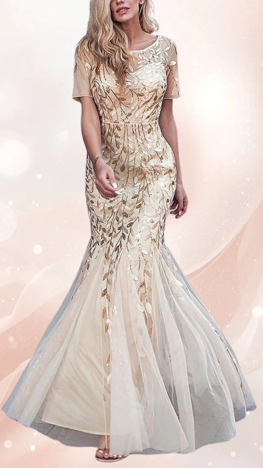 A spring mesh wedding guest dress features a fitted bodice adorned with delicate gold leaf patterns, transitioning into a flowing, semi-transparent skirt. The dress has short sleeves and a mermaid silhouette, complementing its elegant design with a soft, romantic aesthetic. It is styled with light, airy layers, enhancing its movement and sophistication.
