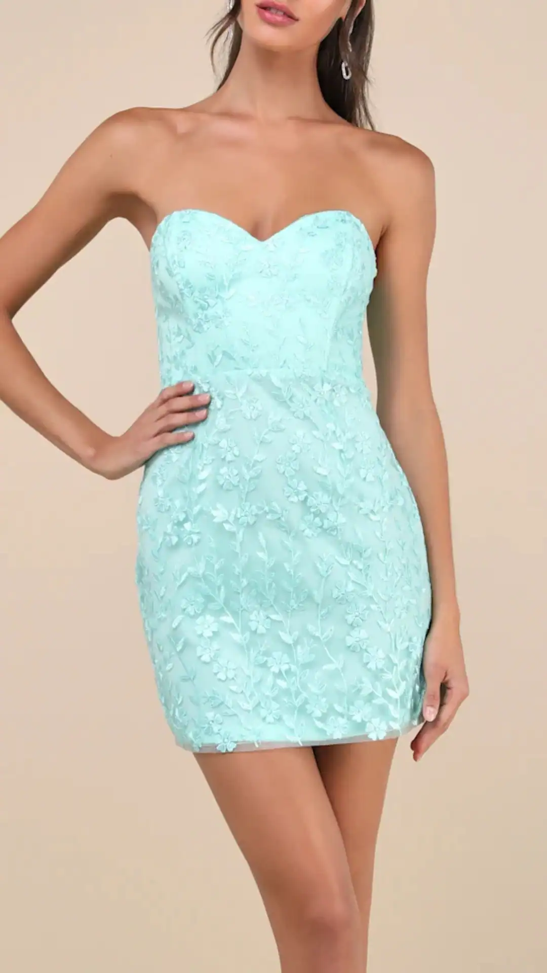This fitted, strapless homecoming dress features a vibrant mint green satin fabric embellished with delicate floral embroidery, creating a soft, textured appearance. Its sleek silhouette hugs the body, showcasing a mini length that captures a chic, youthful vibe, perfect for a lively school dance or party.