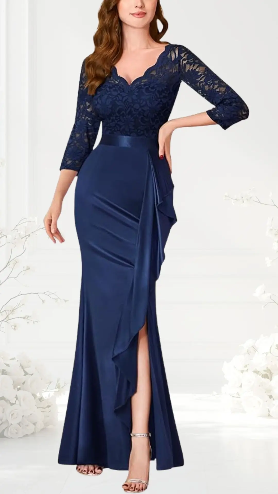 A navy blue wedding guest dress features a fitted silhouette with a lace bodice and three-quarter sleeves. The skirt is made of smooth fabric, cascading down with a side drape and a thigh-high slit for added elegance. The dress is completed with a ribbon at the waist and stylish strappy heels.