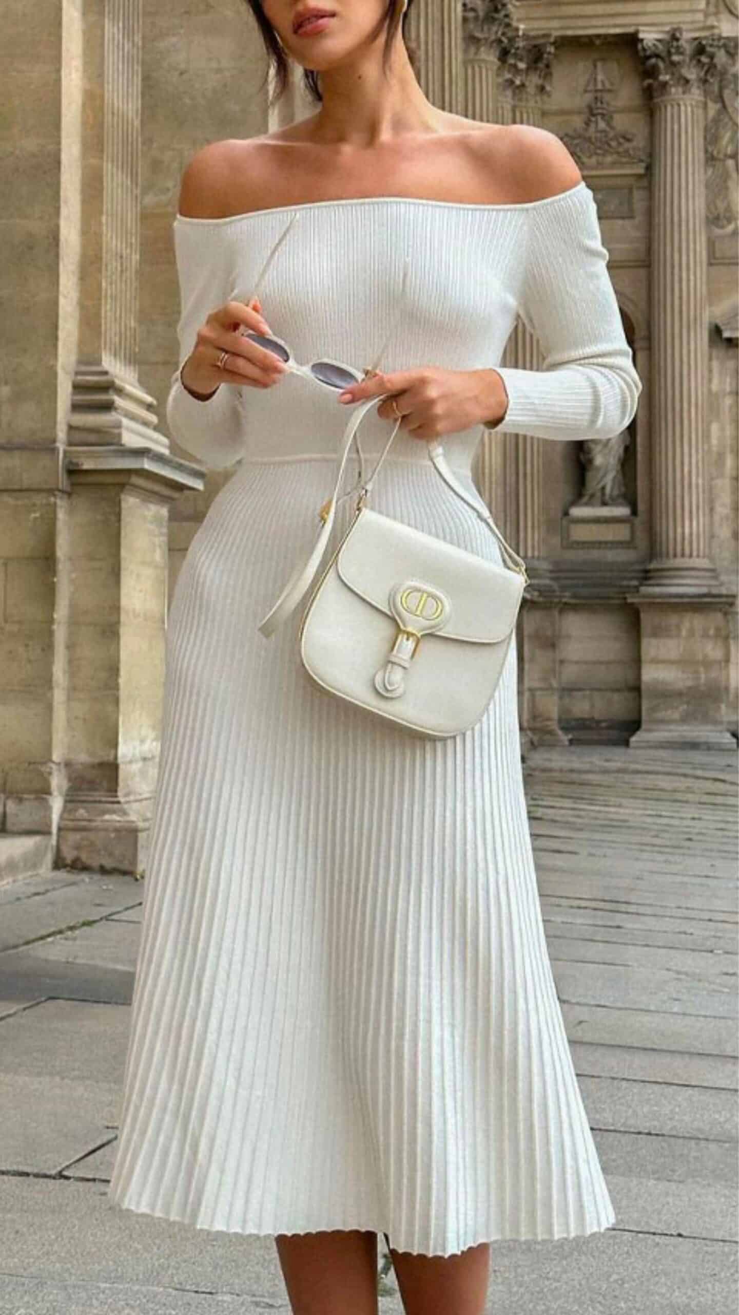 The dress features an off-the-shoulder neckline with long sleeves, a fitted bodice, and a flowing midi skirt that emphasizes a flattering A-line silhouette. Made from a textured ribbed fabric in a soft, pure white, it carries a chic and minimalist vibe, making it suitable for formal occasions or elegant outings.