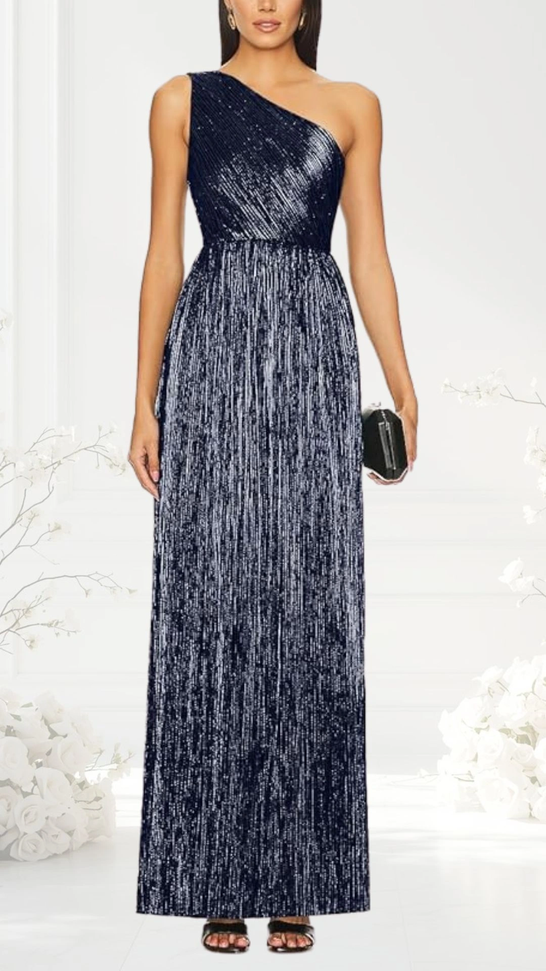 A navy one-shoulder wedding guest dress features a fitted bodice with vertical stripes and a flowing maxi skirt that drapes elegantly down to the floor. The dress is adorned with subtle shimmering textures, enhancing its formal appeal. The model holds a small black clutch, and the background includes soft floral elements, adding a romantic touch.