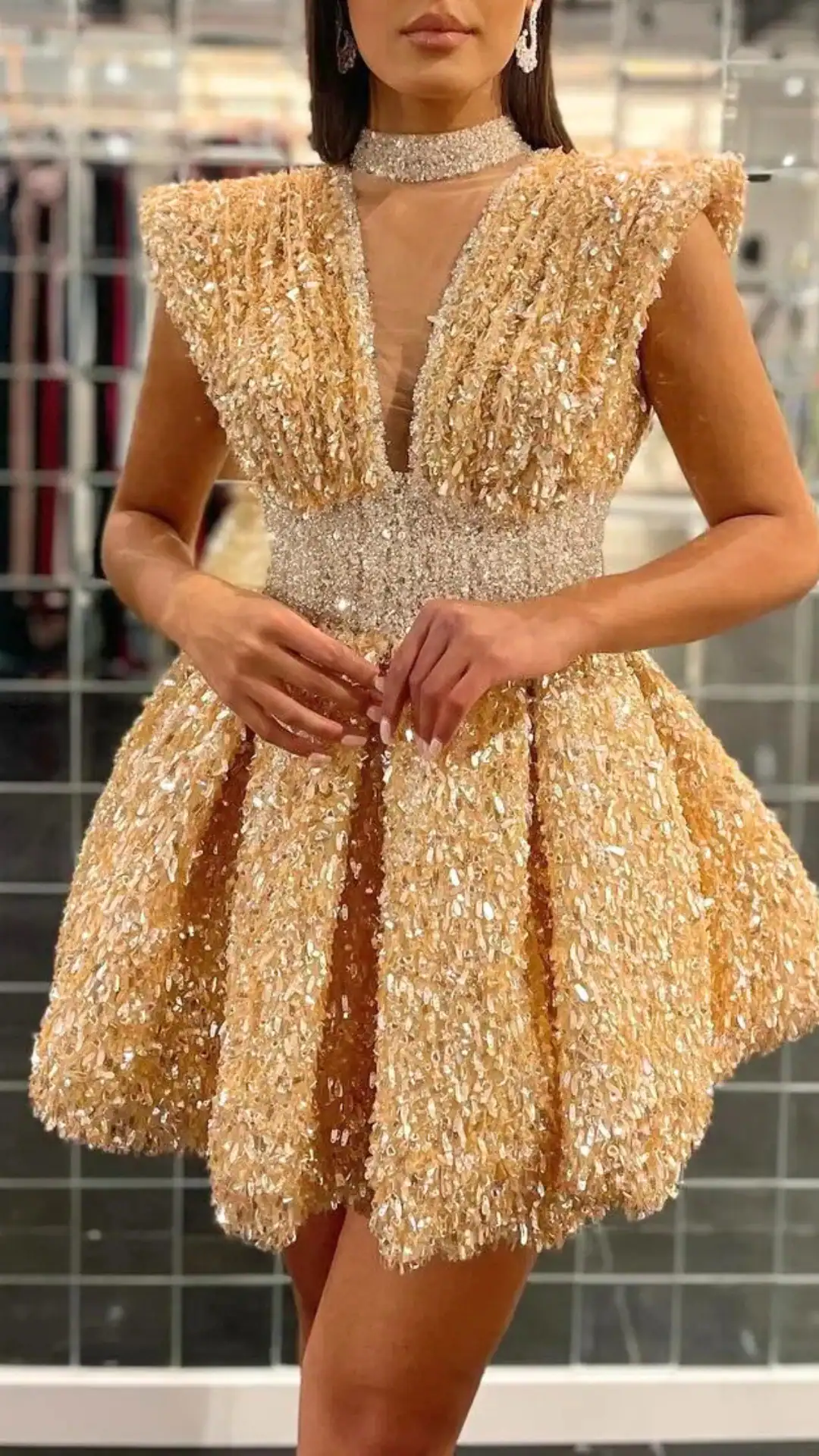 This striking homecoming dress features a voluminous silhouette in a shimmering, pale gold fabric adorned with sparkling sequins, creating a glamorous and eye-catching effect. The design includes elegant cap sleeves, a deep V-neckline, and a cinched waist, exuding a playful yet sophisticated vibe perfect for formal events and school dances, tailored for teenage girls.