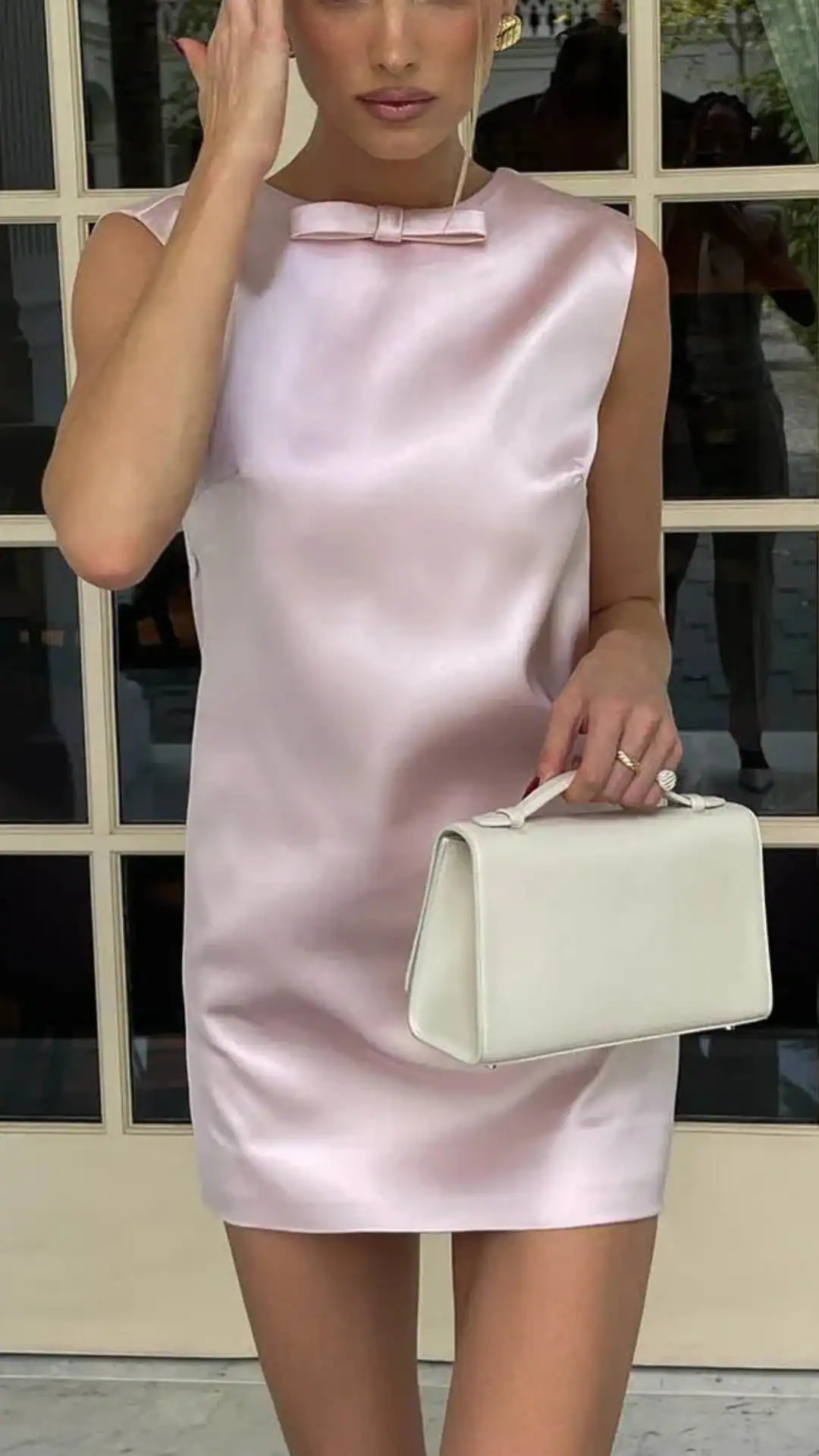 The dress features a sleek silhouette made from smooth, lustrous satin in a soft pastel pink, creating an elegant and fresh appearance. With a minimalist design highlighted by a subtle front bow, this fitted dress is perfect for formal events like homecoming, catering to teenage girls looking for a chic and modern look.