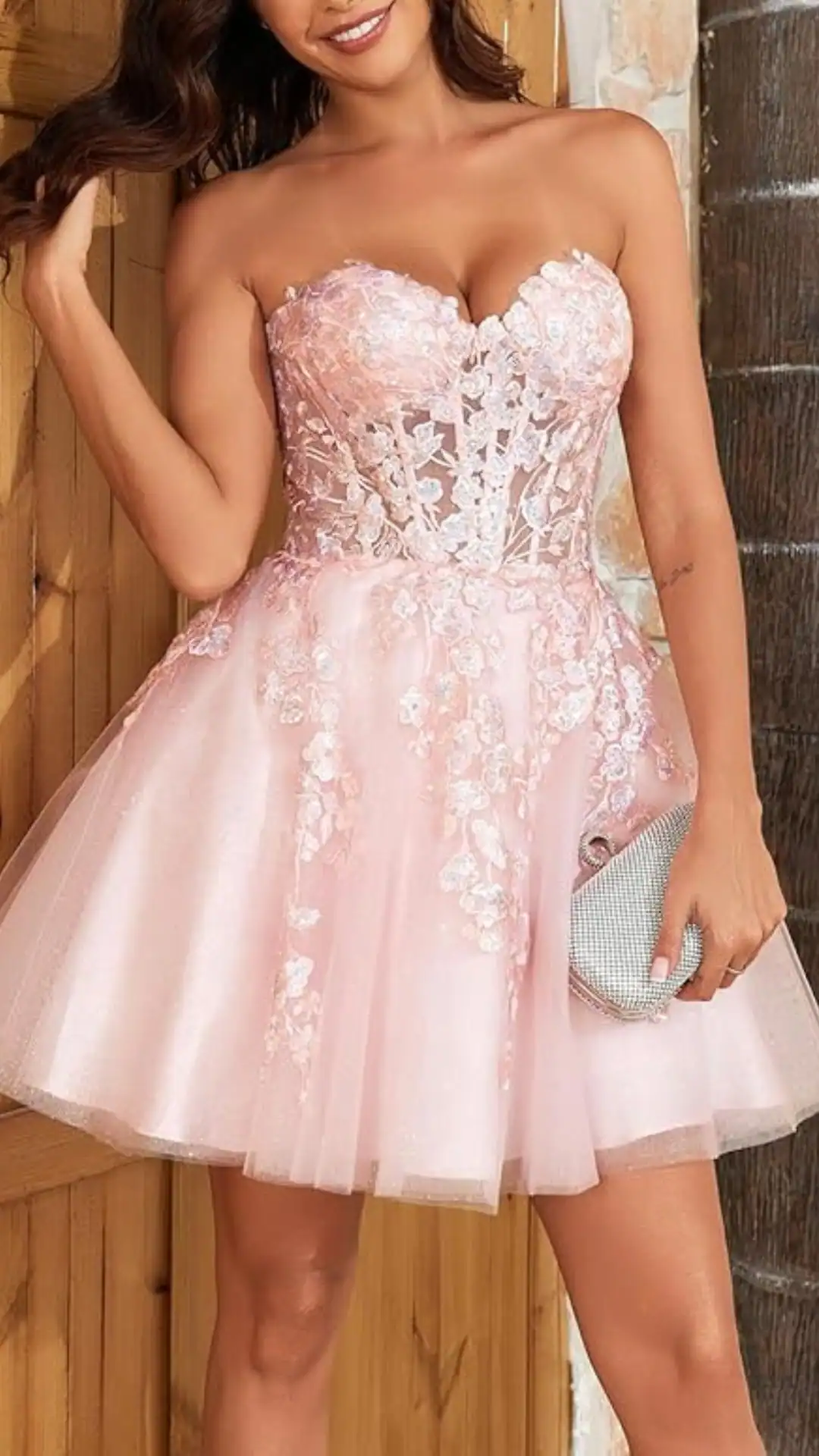 This strapless homecoming dress features a sweetheart neckline and a fitted bodice adorned with delicate floral lace appliqués, transitioning into a flared skirt made from shimmering tulle that adds volume and movement. In a soft pastel pink hue, the overall vibe is romantic and ethereal, making it ideal for formal events and school dances aimed at teenage girls.