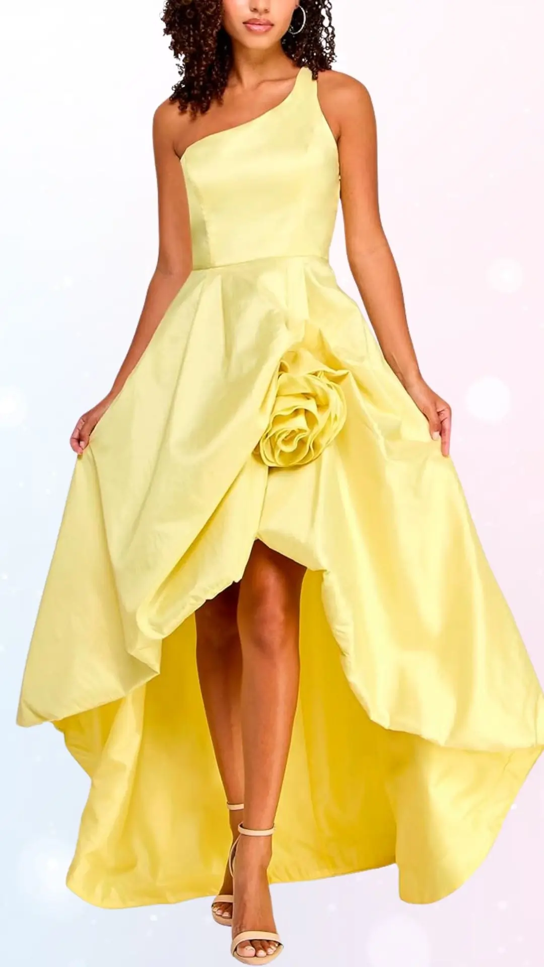 A bright yellow, one-shoulder wedding guest dress features a fitted bodice that flows into a high-low skirt, revealing the legs. The dress is adorned with a large fabric rose on the side, enhancing its feminine look. It is paired with strappy beige heels, creating an elegant and cheerful appearance suitable for spring occasions.