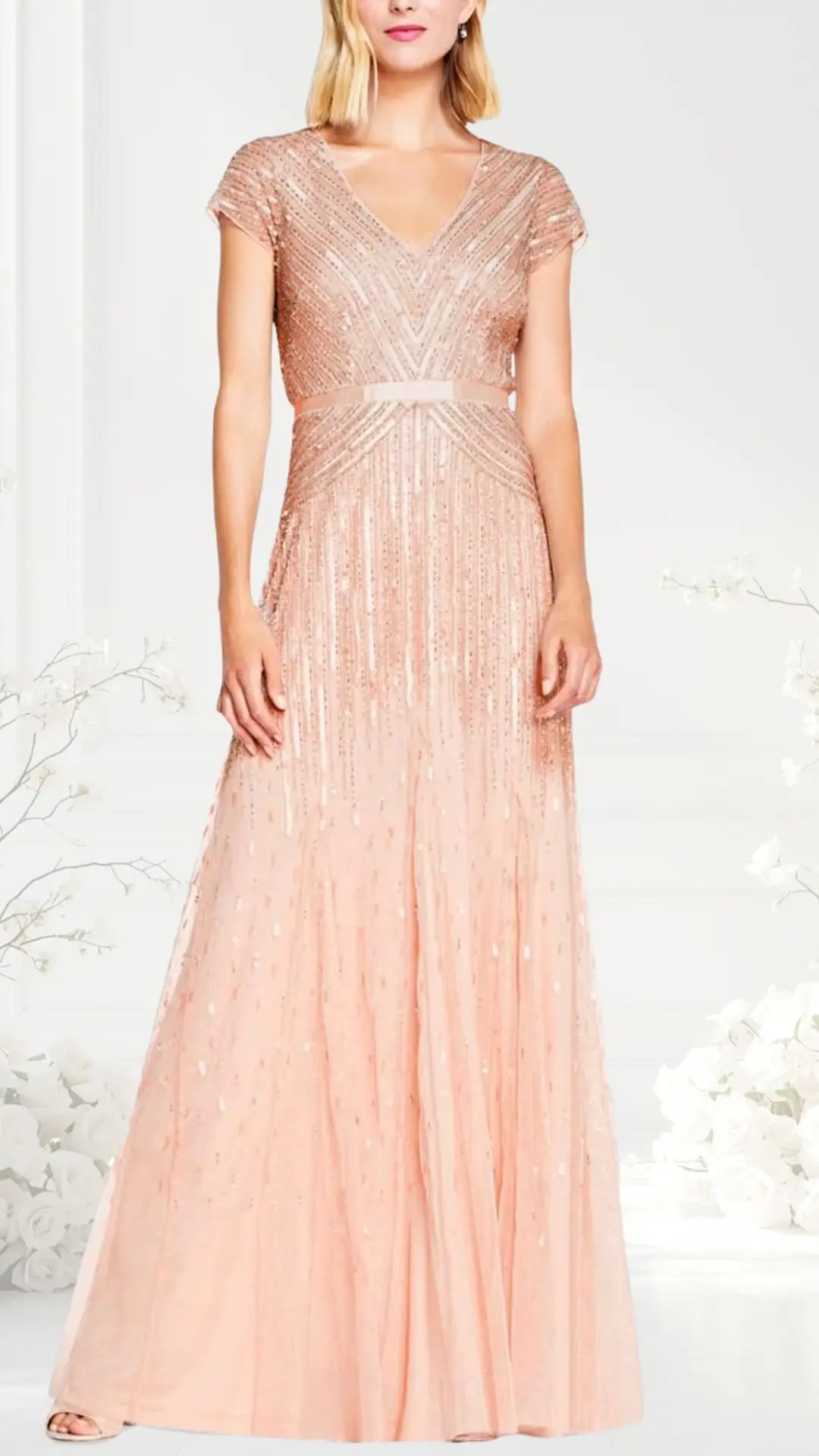 A blush pink wedding guest dress features a flattering V-neckline and short cap sleeves adorned with intricate beadwork that creates a shimmering effect. The gown flows elegantly from the fitted waist, with a soft, sheer skirt embellished with delicate details. This dress combines sophistication and glamor, making it ideal for formal events.