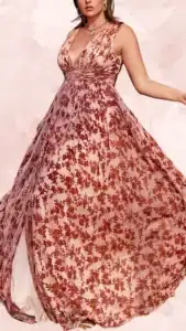This plus-size wedding guest dress features a deep V-neckline and wide straps, providing a flattering silhouette. The flowing maxi length showcases a sheer overlay adorned with intricate rust-colored floral patterns against a soft pink base, creating a romantic and elegant look. A cinched waist gently enhances curves, while the skirt flows gracefully with movement.