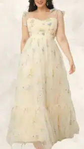 A flowing plus size wedding guest dress features a sweetheart neckline and delicate, sheer tied straps. Crafted from soft tulle adorned with colorful floral embroidery in pinks, yellows, and blues, the dress has a tiered hemline, creating a light and airy silhouette ideal for formal occasions. The overall design balances elegance and comfort, making it a charming choice for any summer wedding.