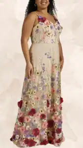 This plus-size wedding guest dress features a delicate, fitted bodice with a deep V-neckline and thin spaghetti straps. The flowing, floor-length skirt is adorned with intricate floral embroidery in shades of pink, purple, and cream, cascading from the bodice to create a vibrant, garden-like appearance. The dress's soft, neutral background highlights the rich colors and adds a romantic, ethereal quality.
