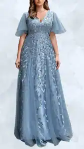 This plus-size wedding guest dress features a flattering V-neckline and sheer flutter sleeves for an elegant touch. The gown is crafted from a soft, draping fabric in a serene blue color, adorned with delicate silver leaf embroidery that adds a sophisticated detail. The full-length design falls gracefully to the floor, creating an ethereal silhouette suitable for formal occasions.