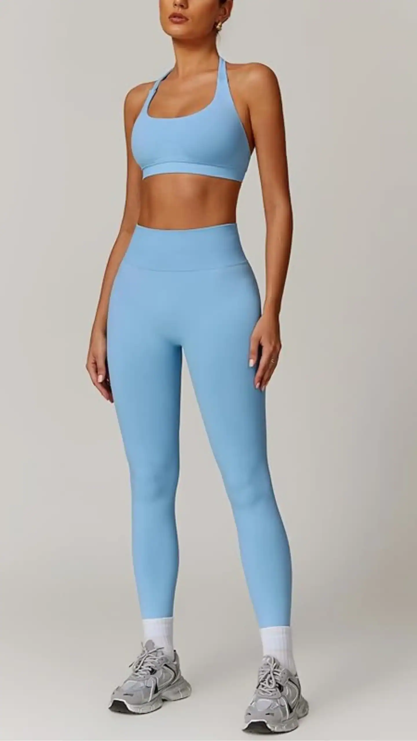 A seamless two-piece workout set in a soft, powder blue color, featuring a ribbed high-waisted legging and a supportive halter neck sports bra. The stretchy polyamide-elastane fabric offers a snug fit with tummy control, ideal for various fitness activities while ensuring comfort and style.