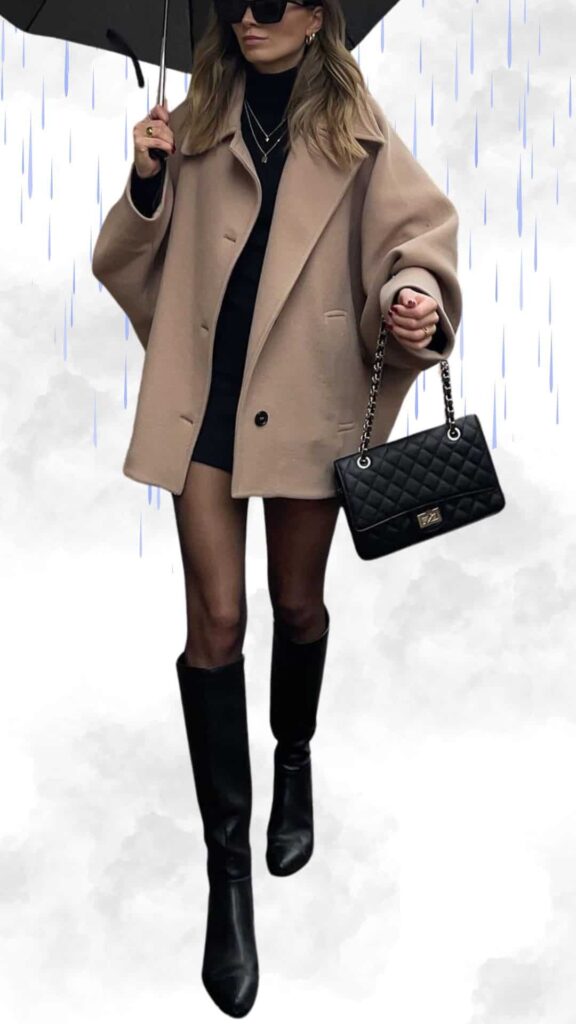 The outfit features a soft, beige oversized coat layered over a fitted black turtleneck, creating a chic contrast. Paired with sleek black knee-high boots, the look is polished and elegant, further complemented by a structured black quilted handbag and delicate layered necklaces. An umbrella completes the ensemble, making it both stylish and practical for rainy weather.